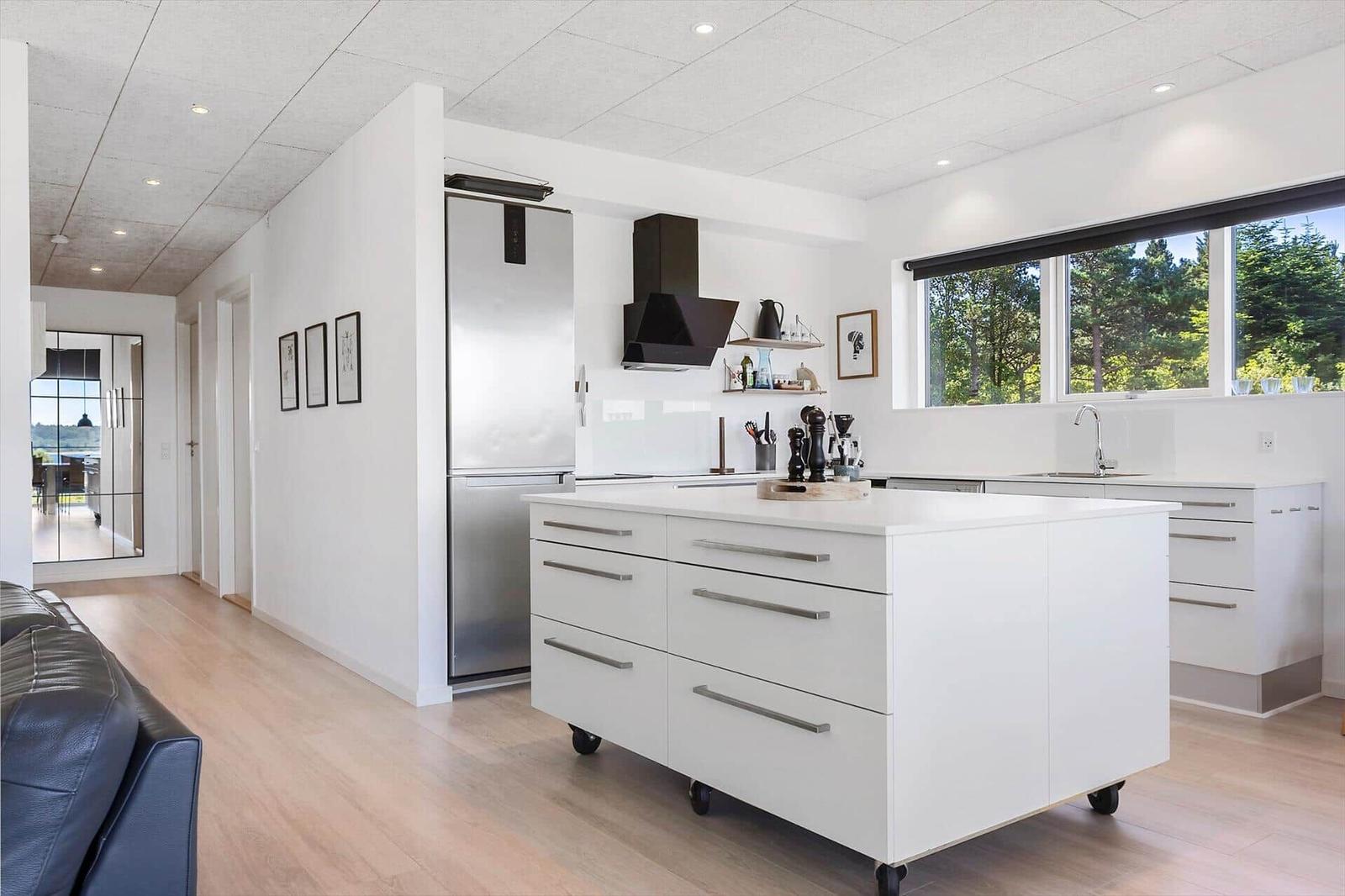 Moderne Küche mit weißer Arbeitsplatte, Edelstahl-Kühlschrank und Blick auf Wald.