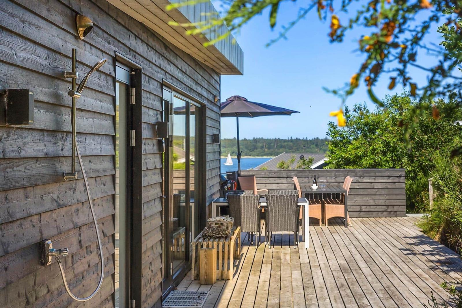 Terrasse mit Dusche an der Wand, Sitzgruppe und Blick auf Wasser.