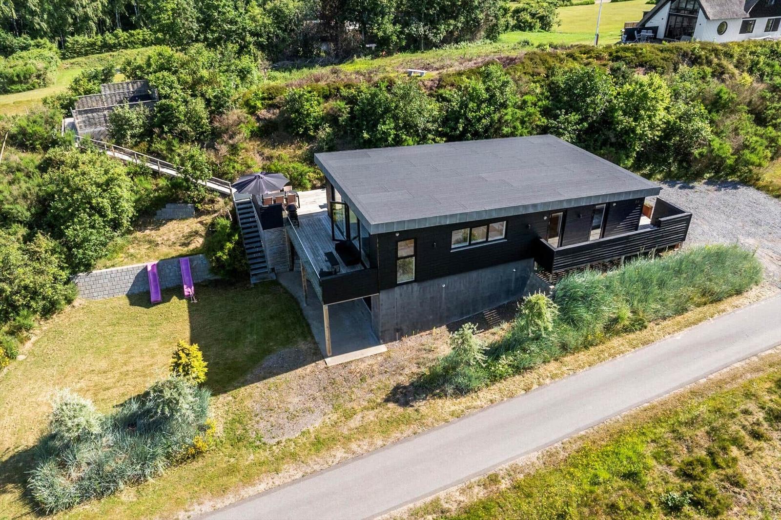 Moderne schwarze Hütte mit Terrasse, Garten und Waldumgebung.