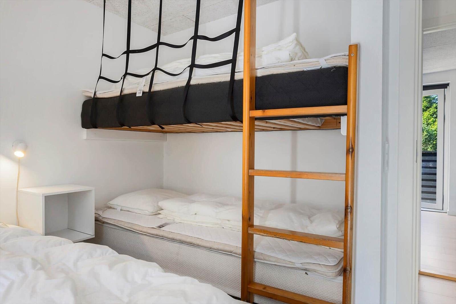 Doppelstockbett mit Matratzen und Leiter. Neben einem Bett steht ein Nachttisch.