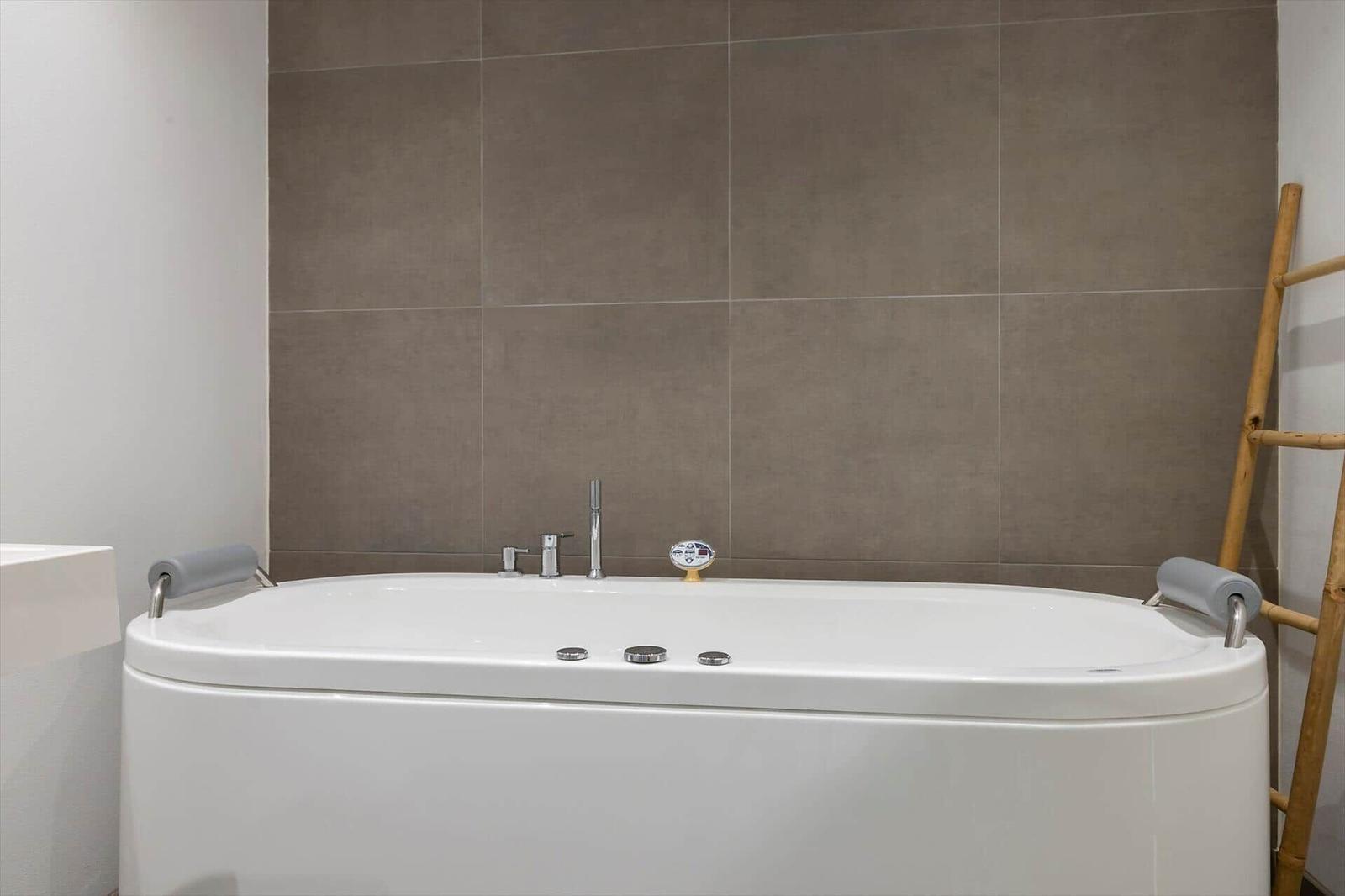 Eine weiße Badewanne mit Armlehnen und Duschkopf an der Wand
