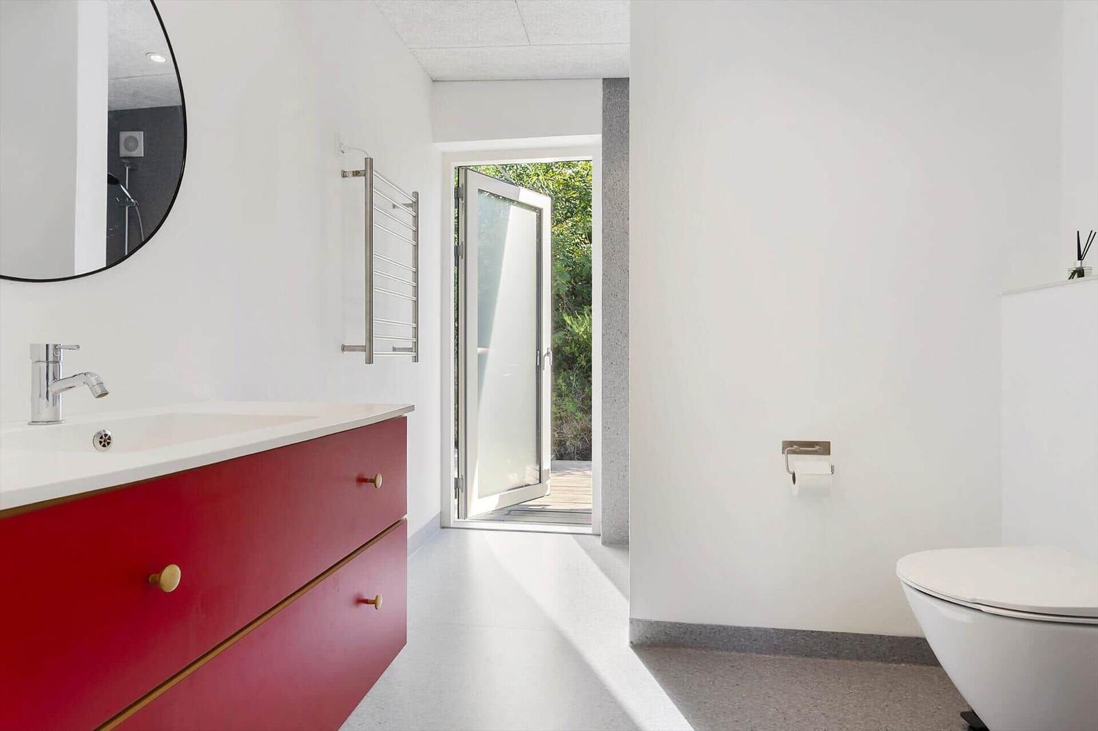 Badezimmer mit rotem Waschbeckenunterschrank, Spiegel und Tür zum Garten.