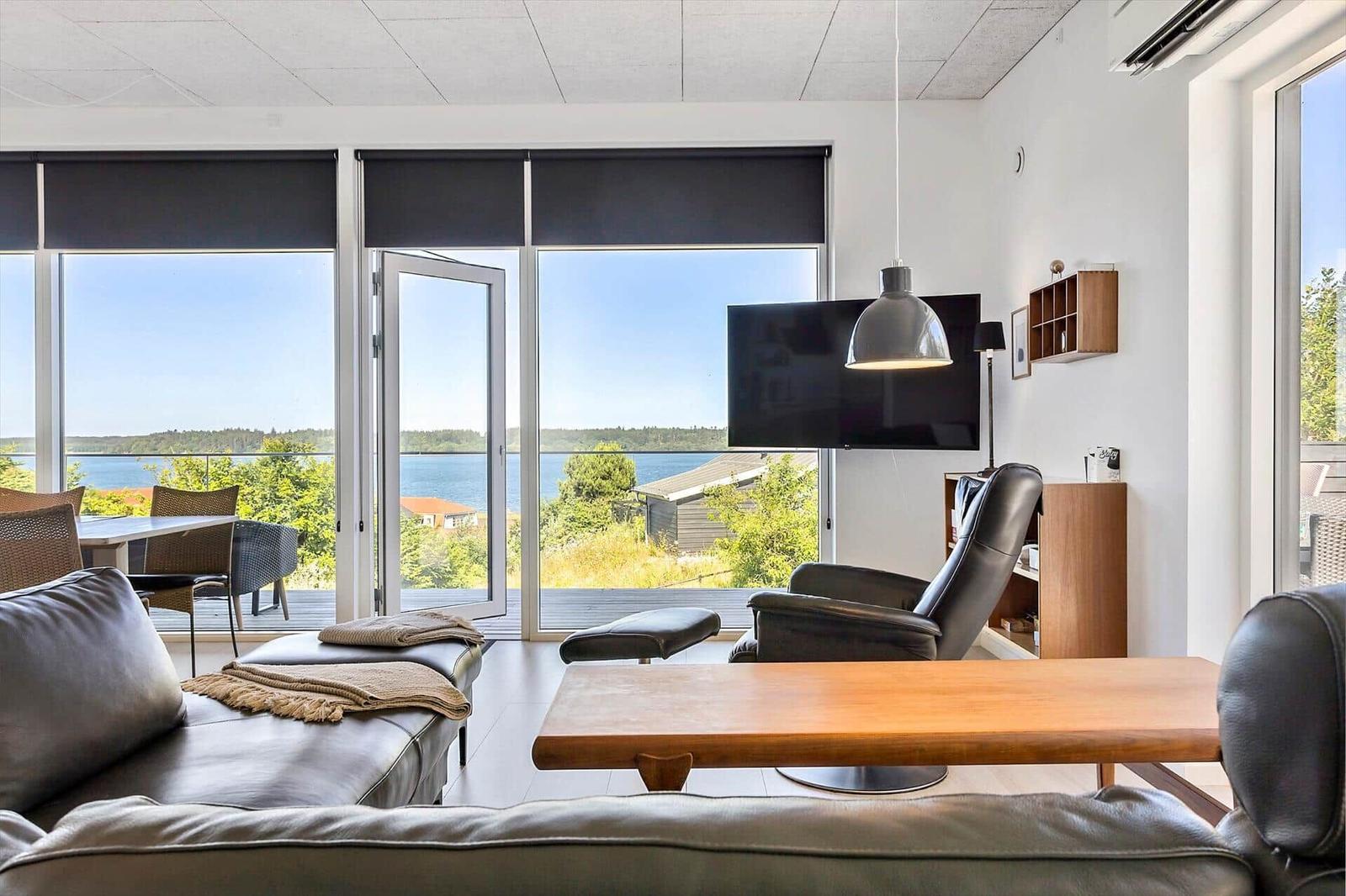 Wohnzimmer mit Aussicht auf Wasser und Garten. Sofa, Couchtisch und Fernseher.