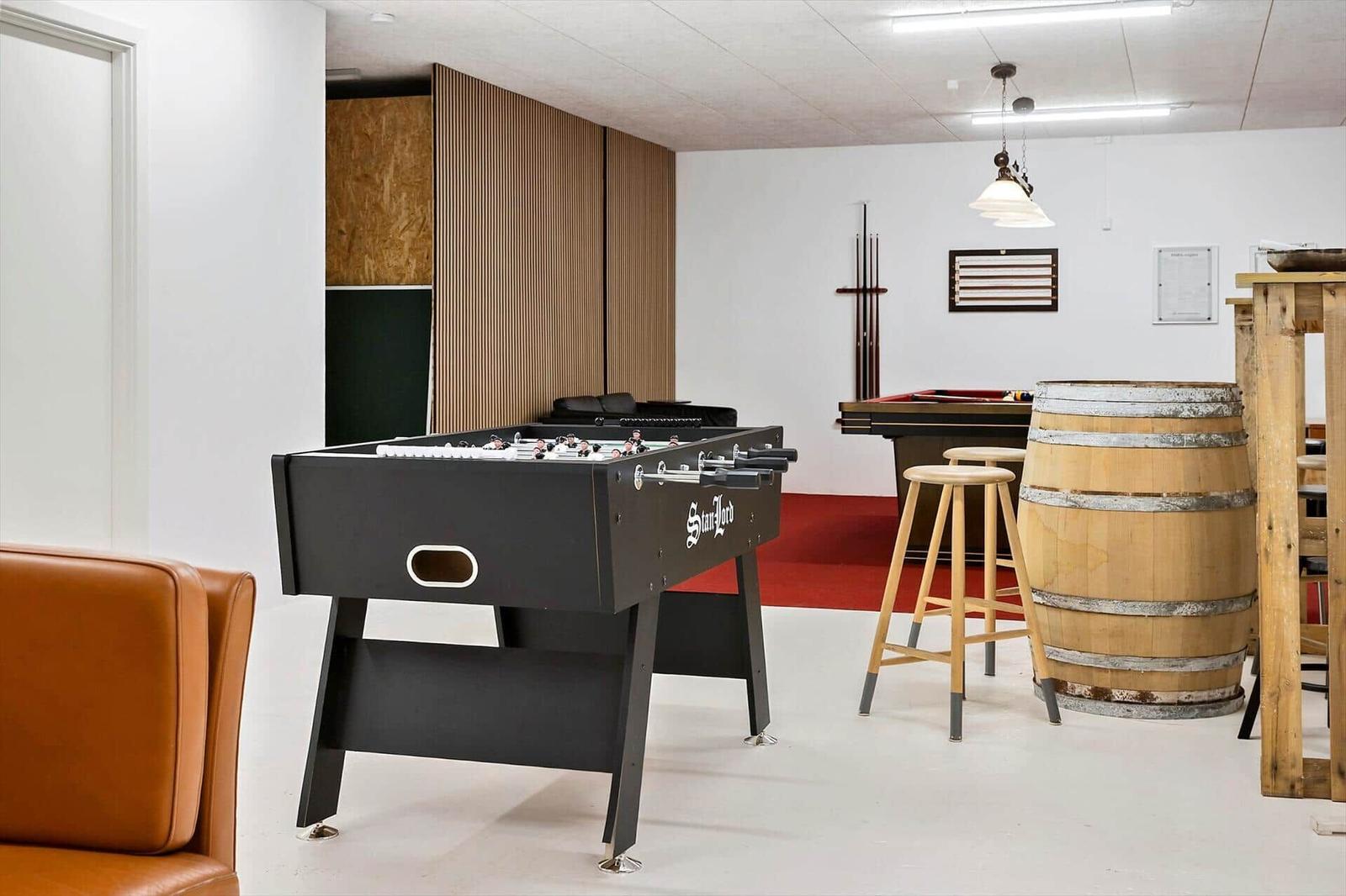 Ein Raum mit Tischfußball, Billardtisch, Holzfass und Stühlen.