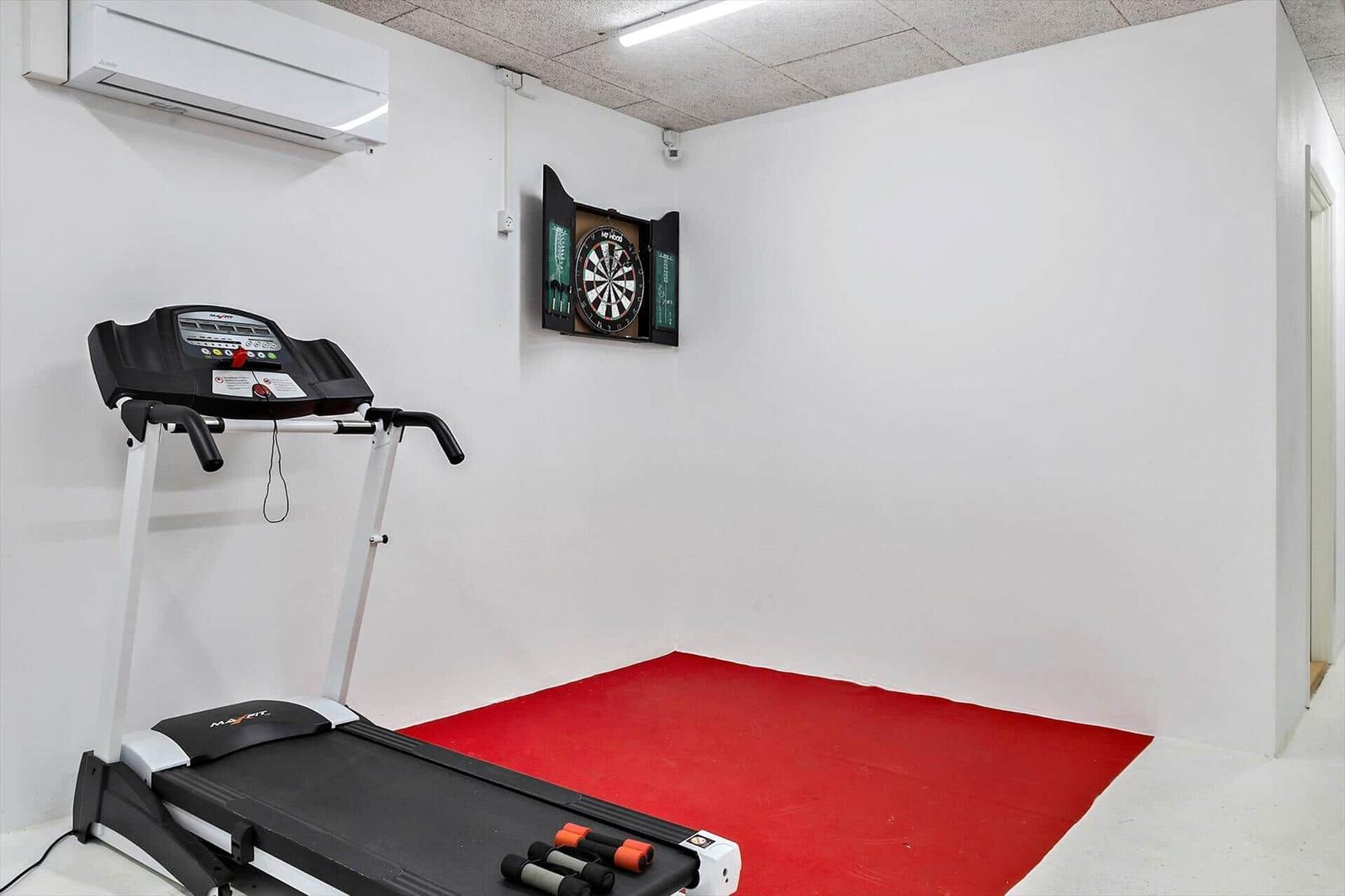 Fitnessraum mit Laufband und Dartboard auf rotem Boden
