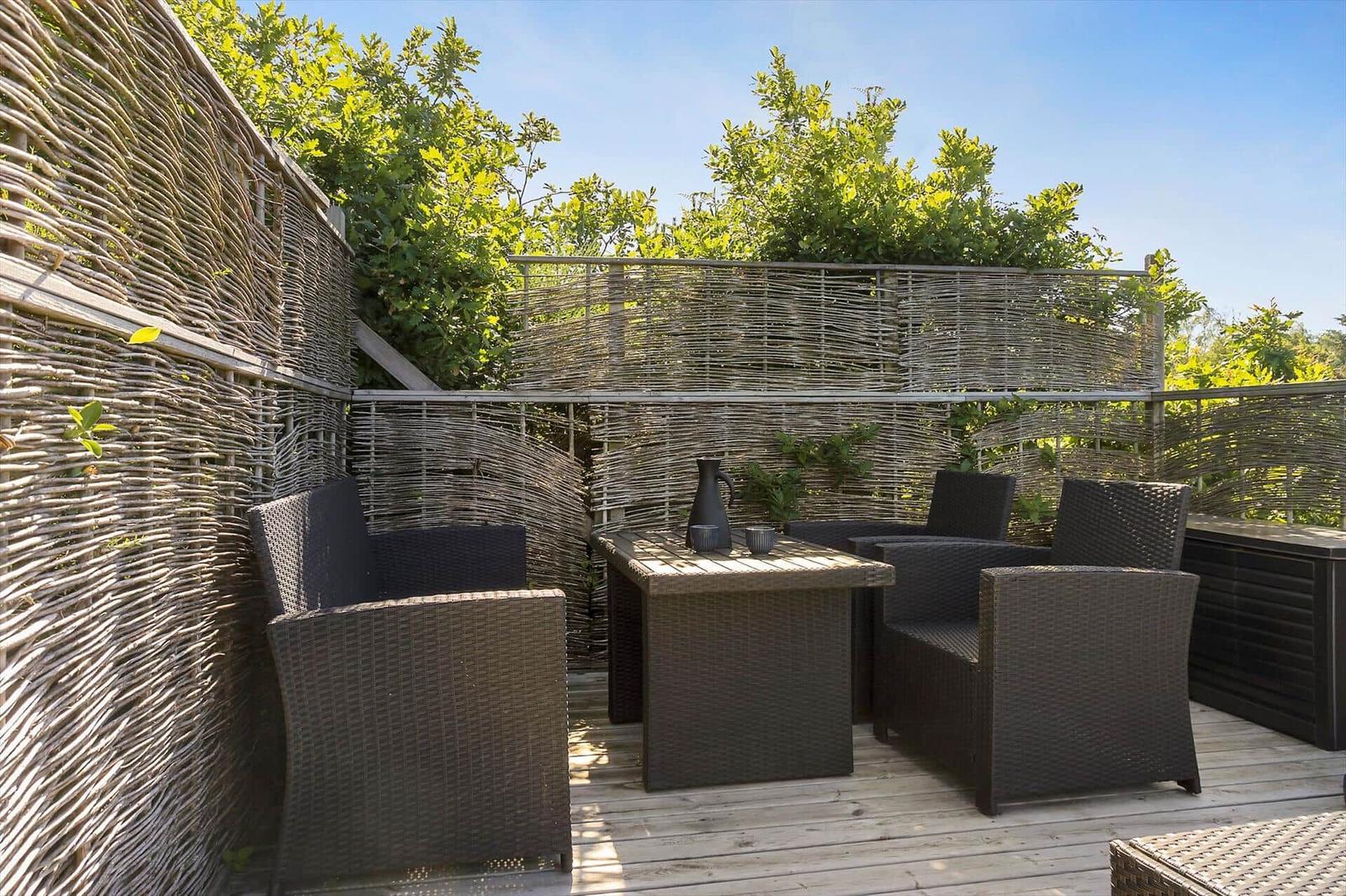 Terrasse mit Gartenmöbeln und Wicker-Zaun. Holzdecke und grüne Pflanzen im Hintergrund.