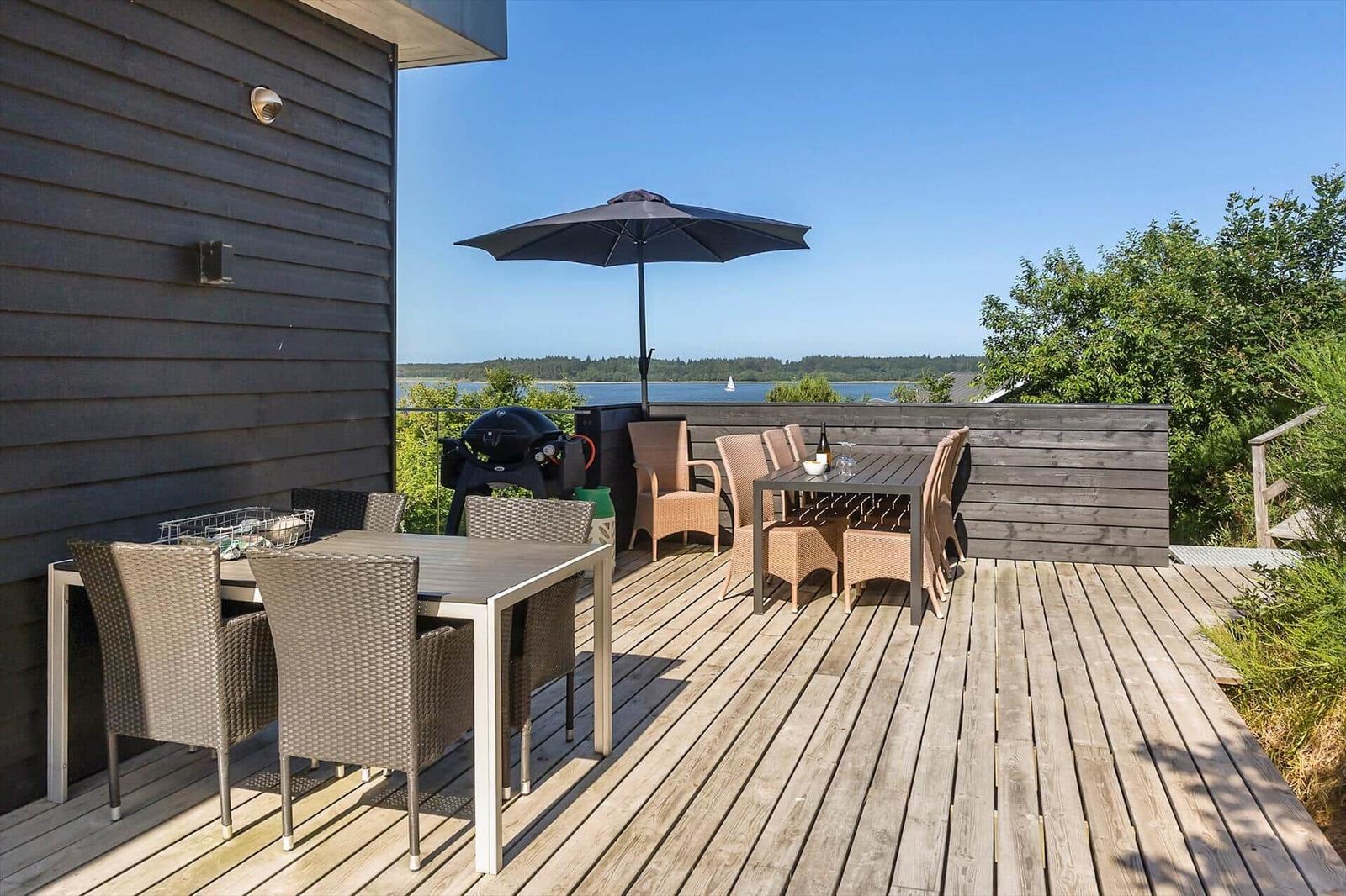 Terrasse mit Essbereich, Grill und Blick auf Wasser und Wald.