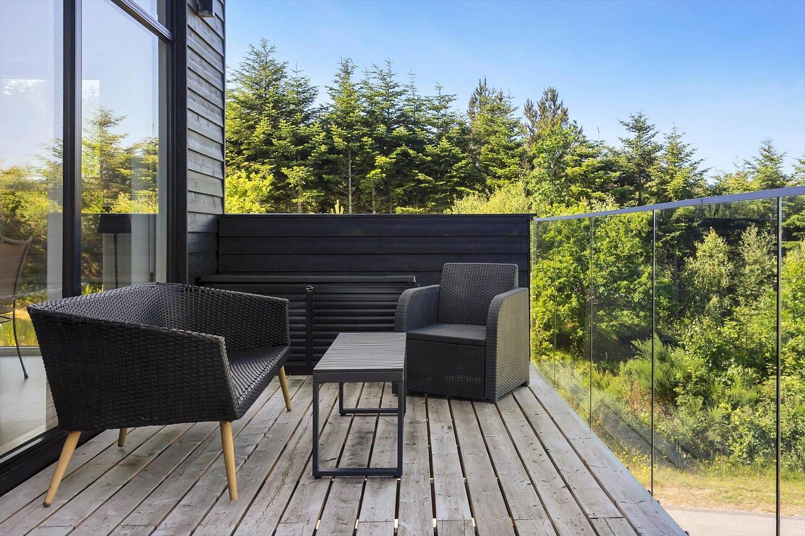 Terrasse mit zwei Sesseln und Tisch, Blick auf Wald und Himmel.