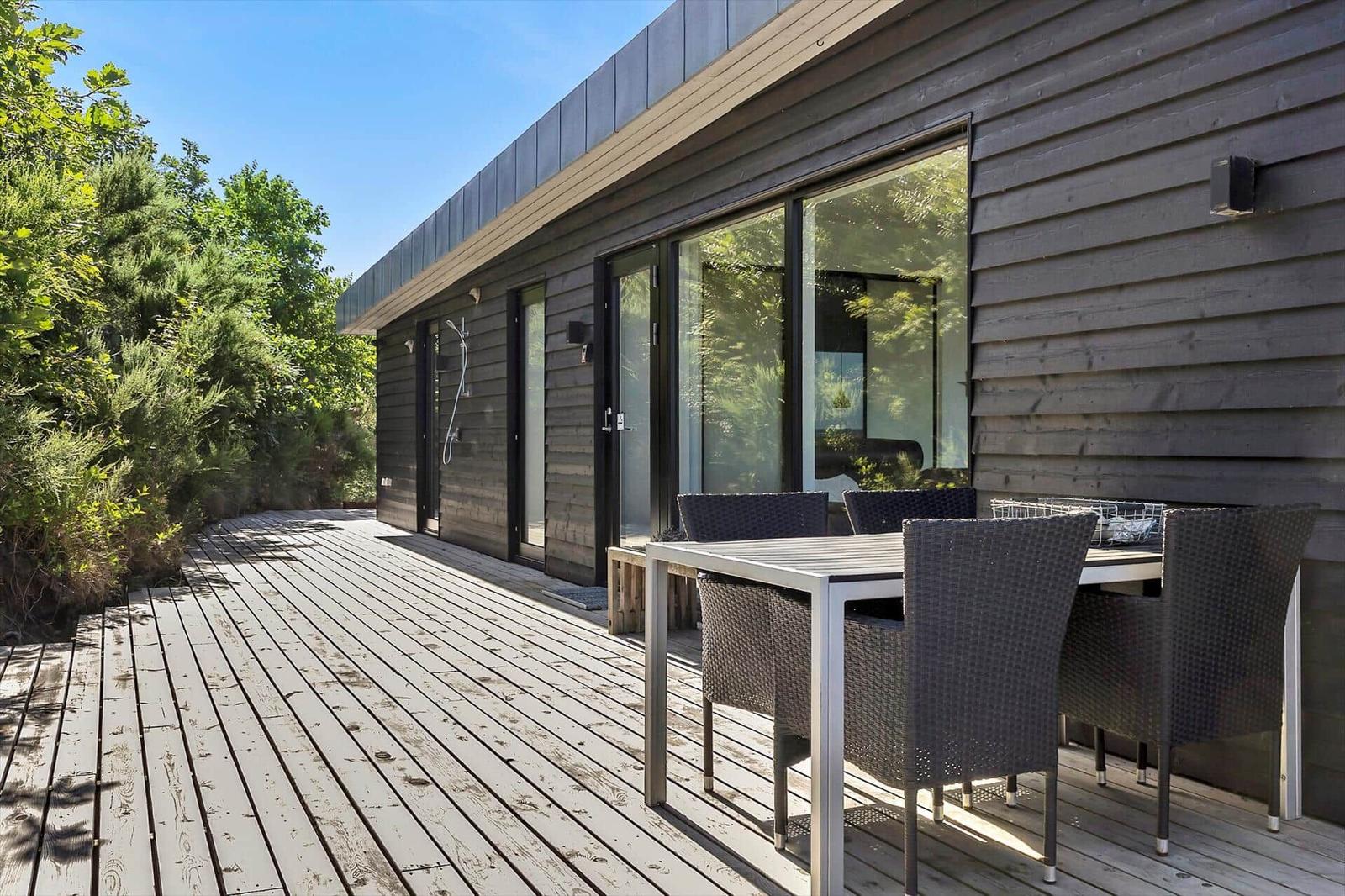 Terrasse mit Tisch und Stühlen neben modernem Holzhaus mit großem Fenster