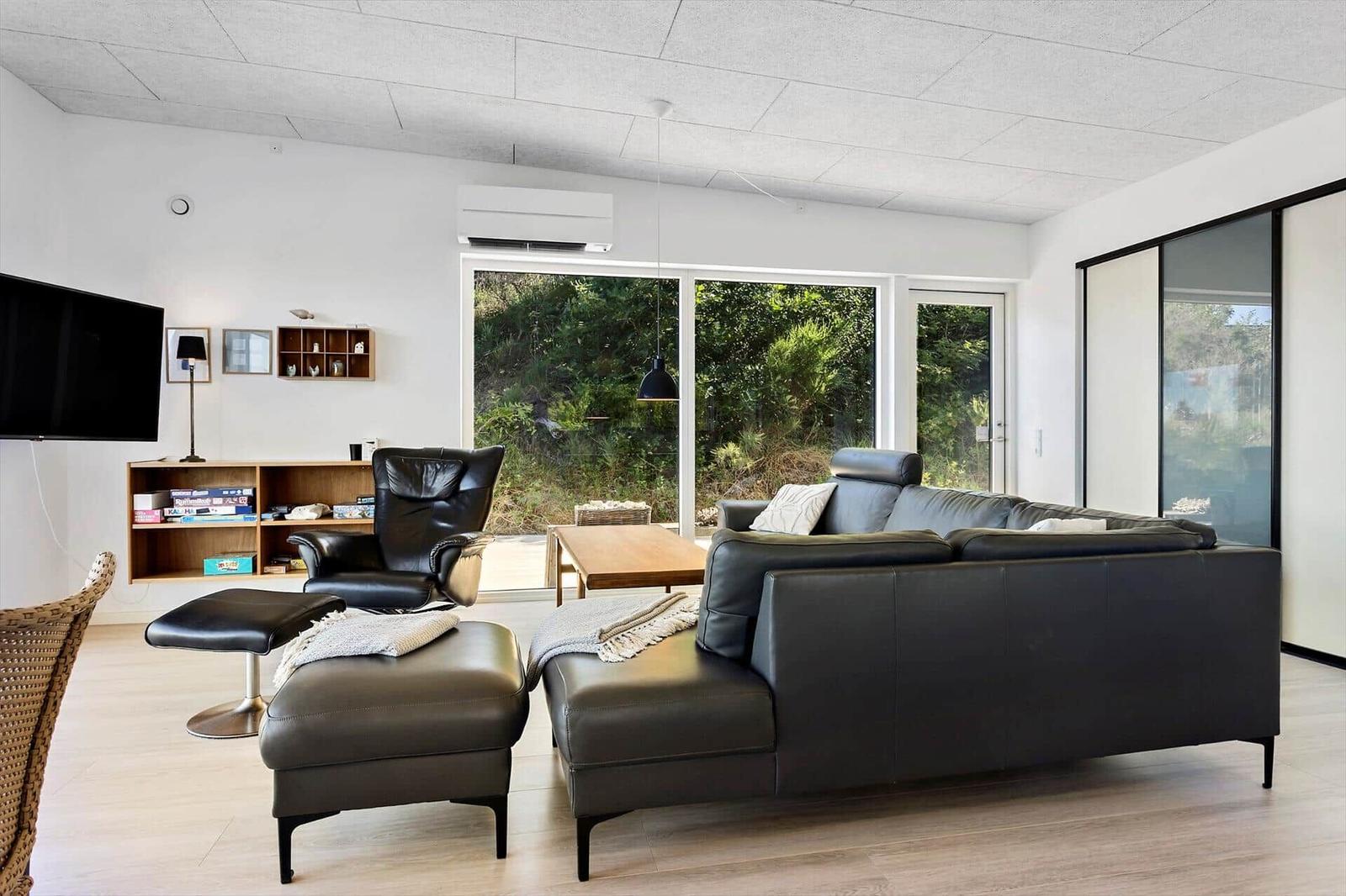 Wohnzimmer mit schwarzer Ledercouch, Sessel und Holztisch. Große Fenster und Glaswand.