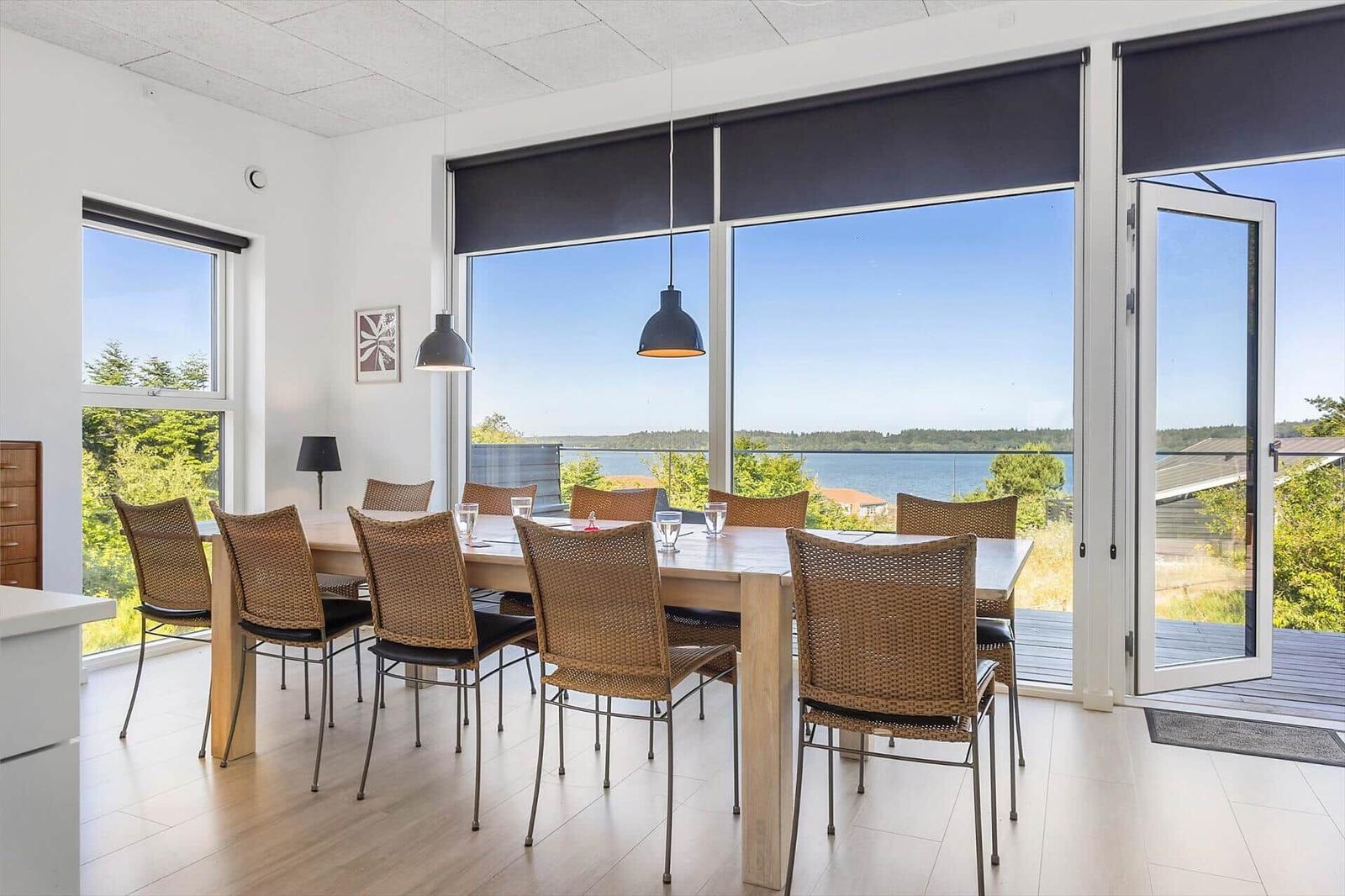 Essbereich mit Tisch und Stühlen. Große Fenster mit Blick auf Wasser und Wald.