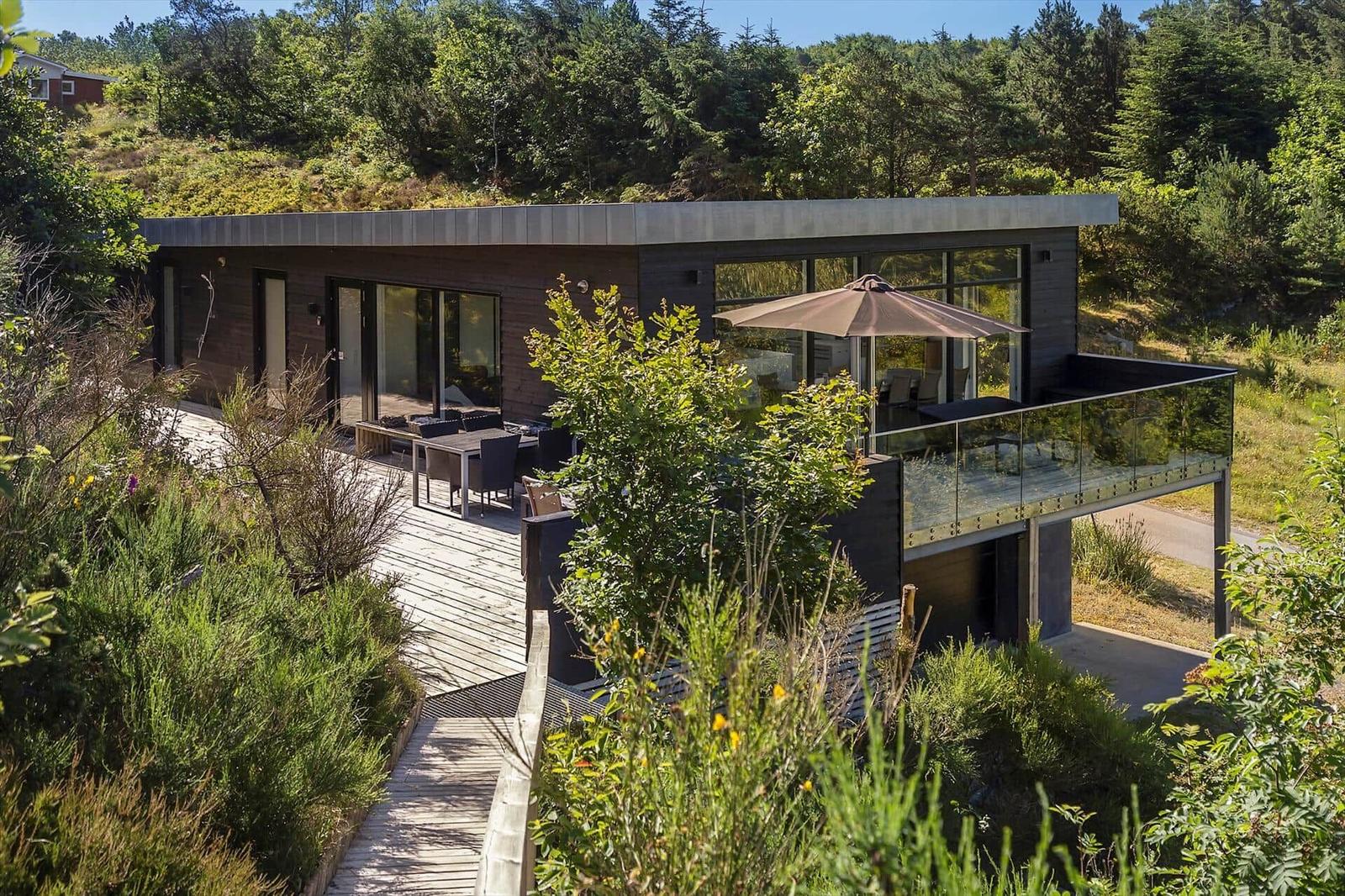 Moderne Villa mit Terrasse und Garten. Holzterrasse, Glasgeländer und Sonnenschirm.