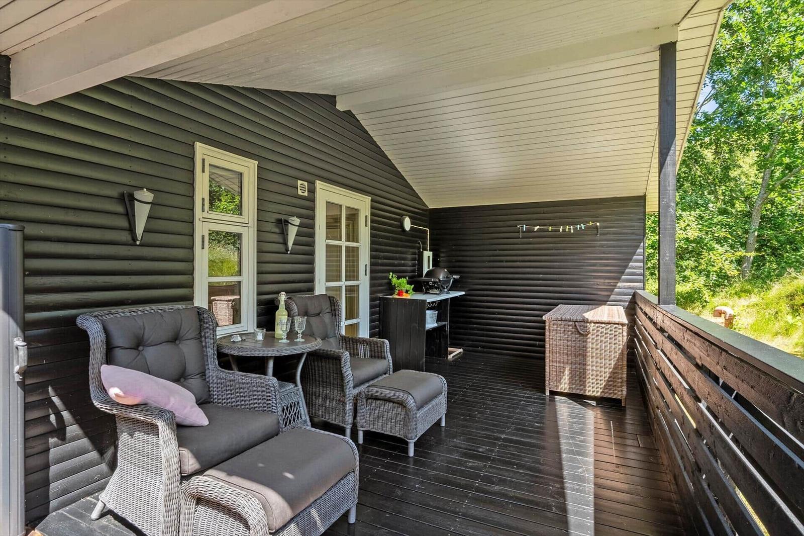 Terrasse mit Sitzgruppe, Grill und Holzgeländer. Dunkle Holzwand und Sonnenschutz.