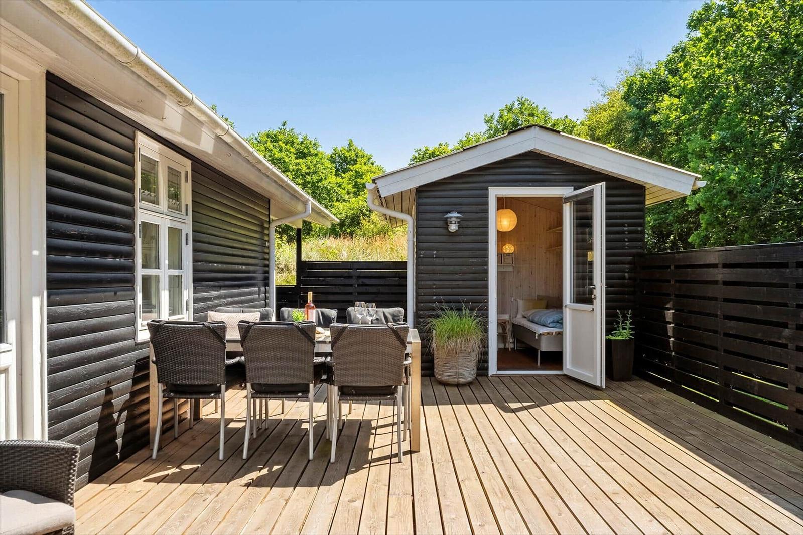 Terrasse mit Sitzgruppe, Blick in Schlafzimmer, umgeben von Bäumen und Holzgeländer.