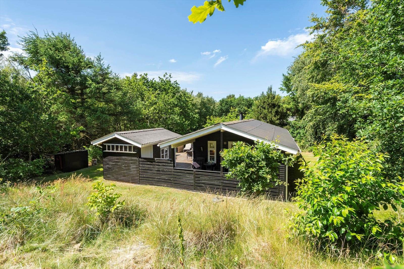 Holzhaus mit Terrasse im Grünen. Umgeben von Bäumen und Gras.