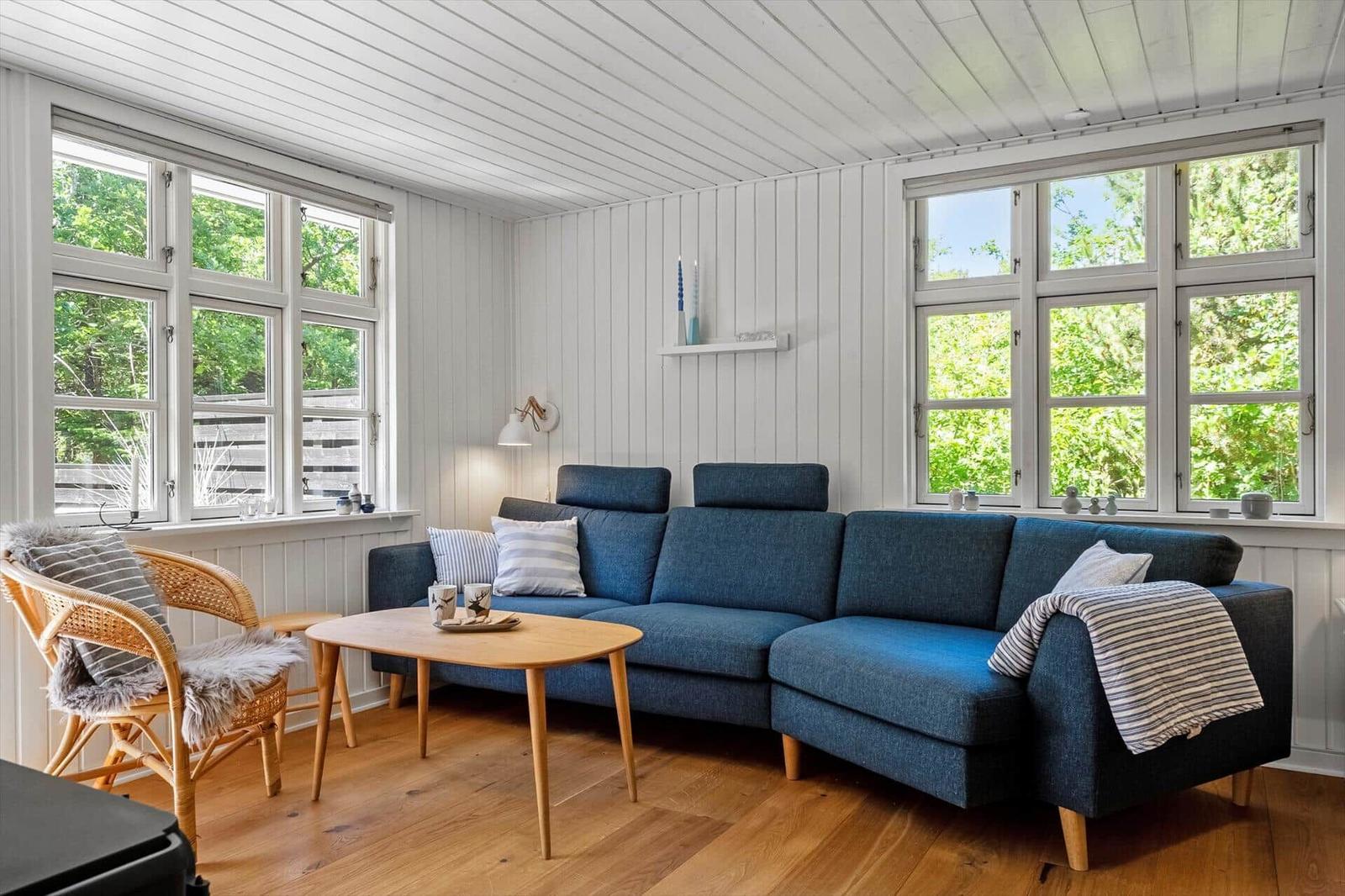 Ein Wohnzimmer mit blauem Sofa, Holztisch und großen Fenstern. Holzfußboden und weiße Wände.