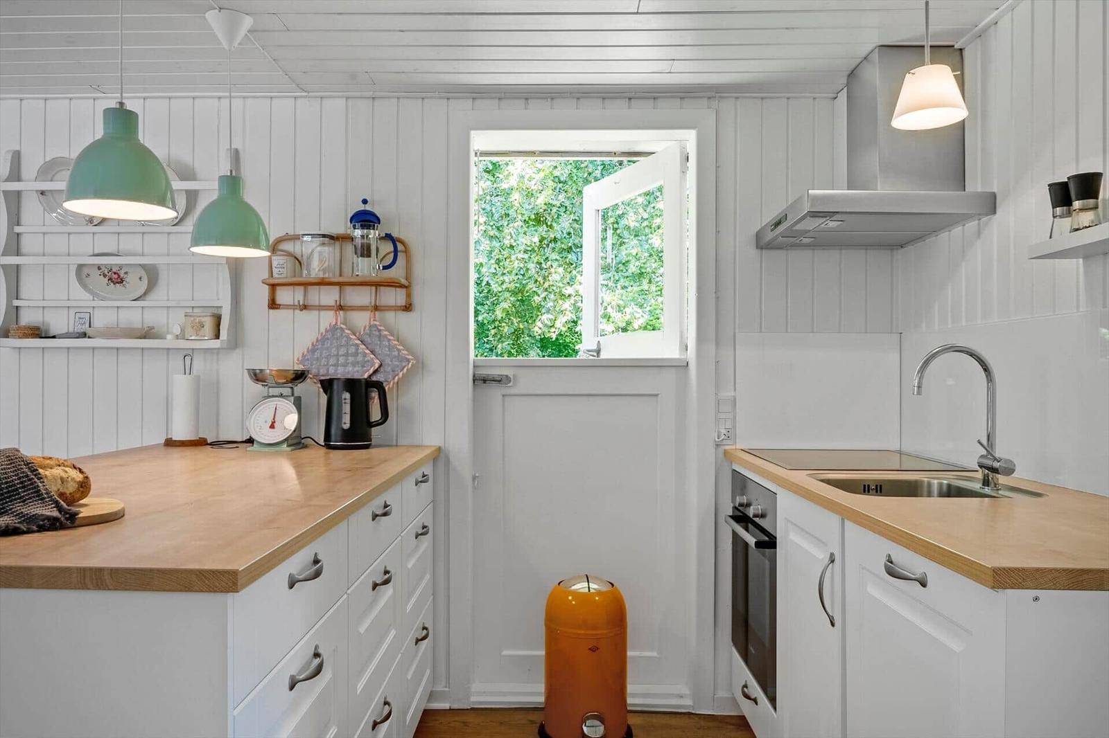 Küche mit Holzplatte, weißen Schränken und Fenster zum Garten.