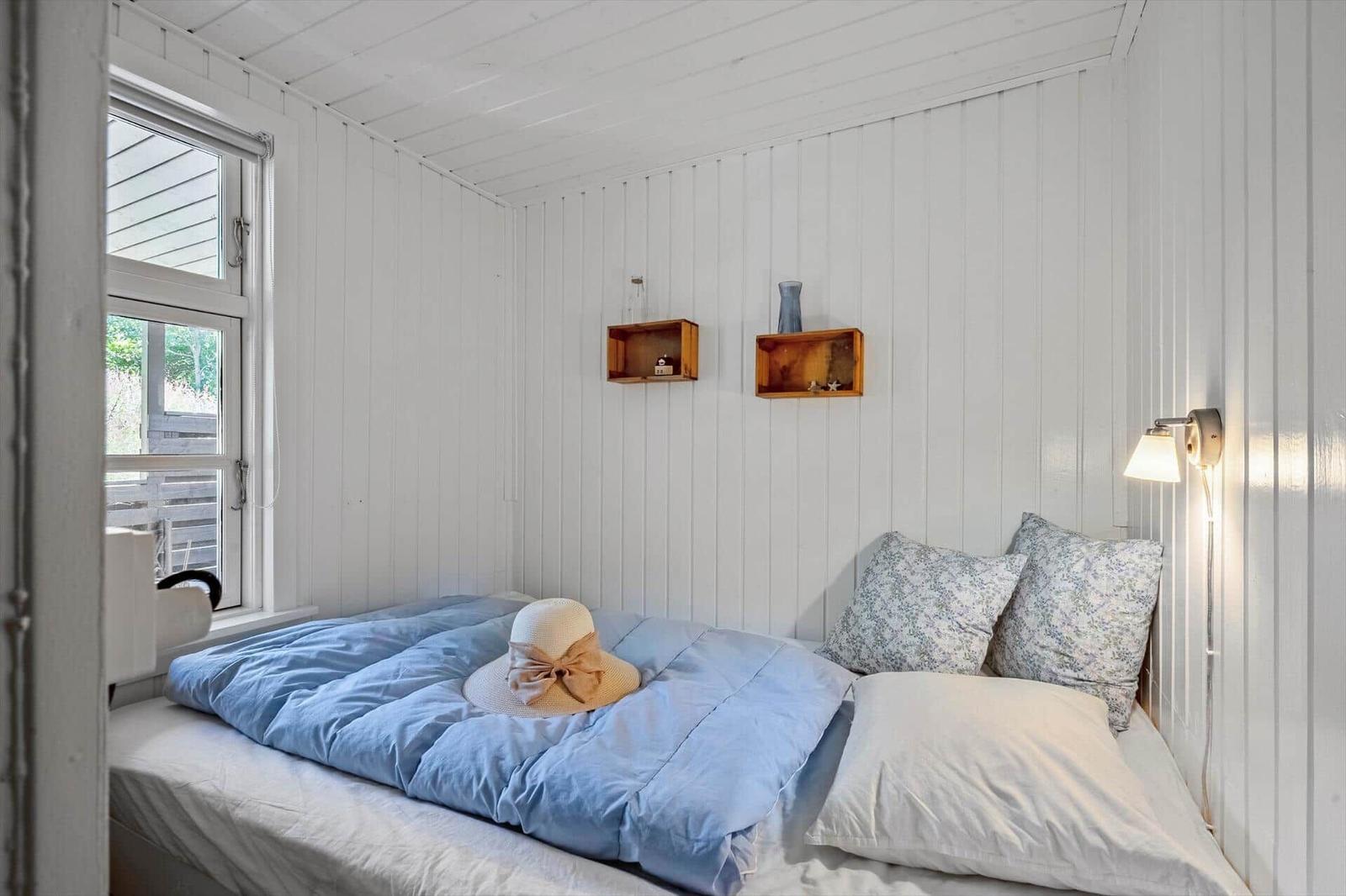 Ein Schlafzimmer mit weißer Holzwand, Bett mit blauer Bettdecke und einem Hut darauf.