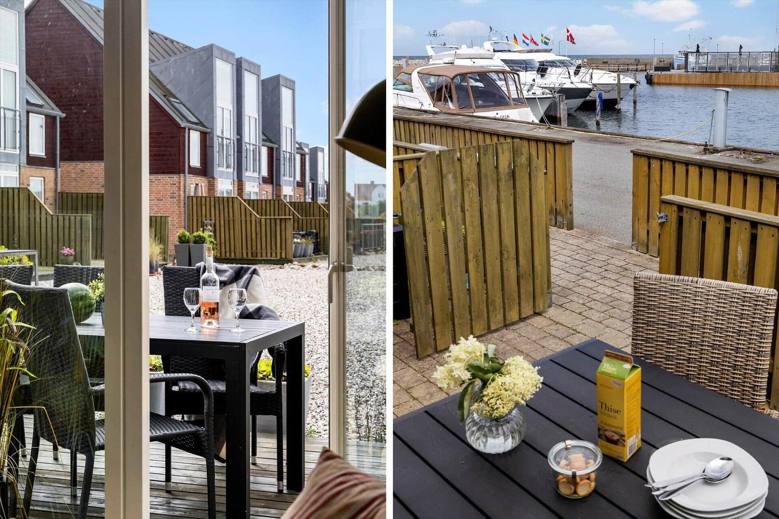 Terrasse mit Tisch und Stühlen, Blick auf Häuser und Hafen mit Booten.