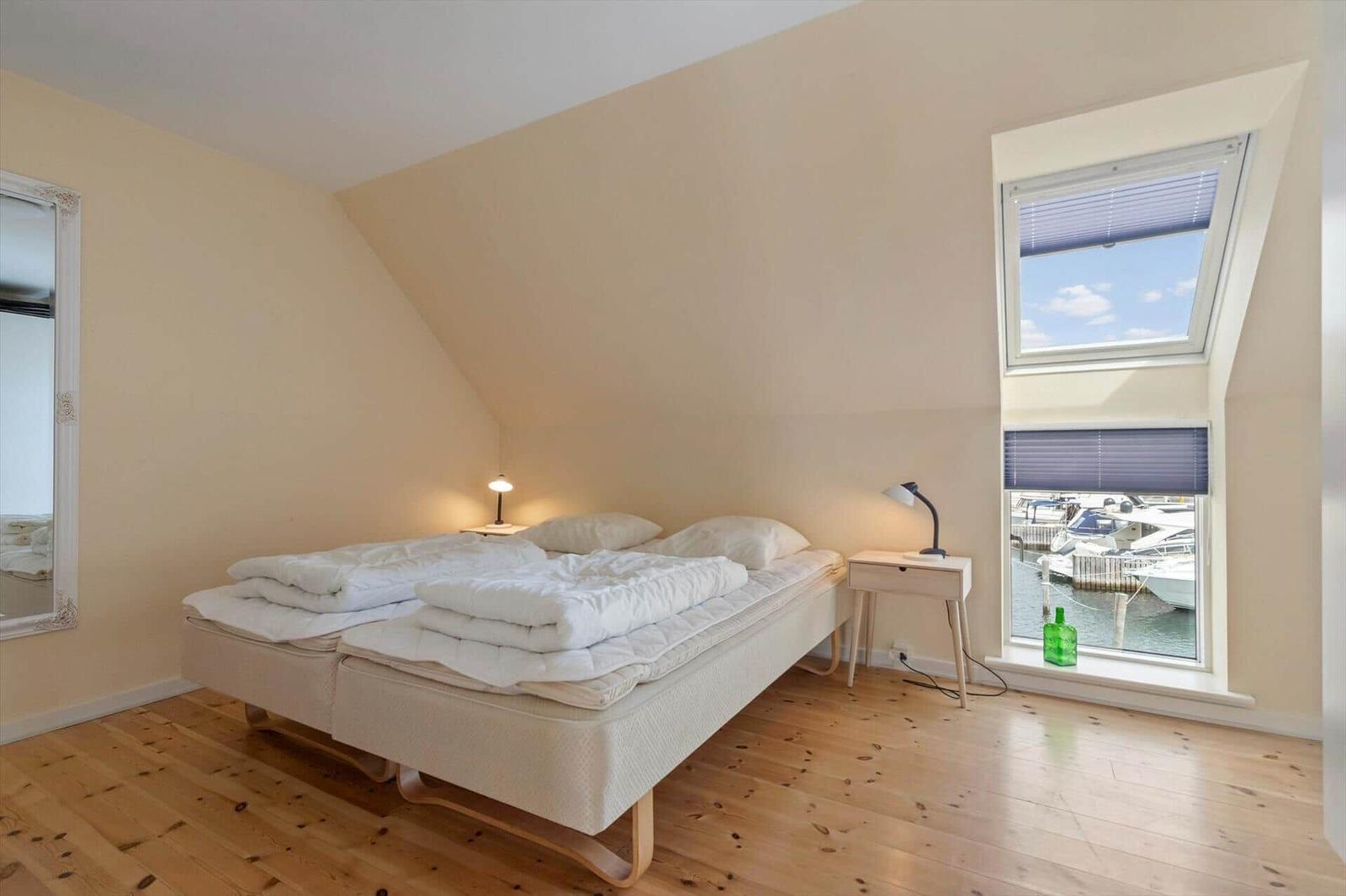 Schlafzimmer mit Doppelbett, Fensterblick auf Hafen und Holzboden.