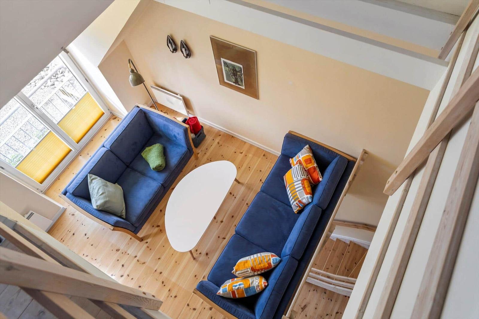 Zwei blaue Sofas mit Kissen, weißer Tisch und Holzboden im Wohnbereich.