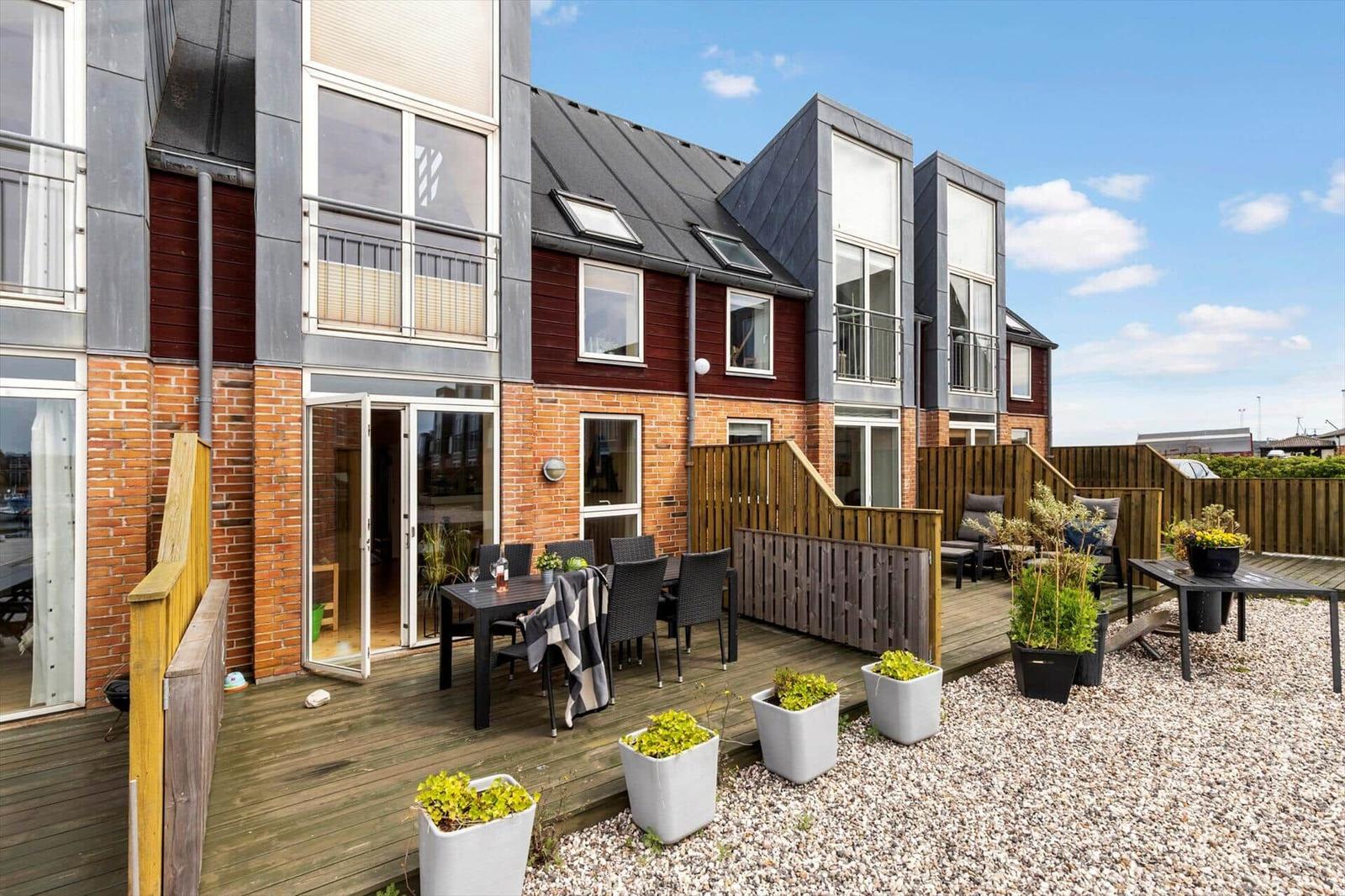 Terrasse mit Tisch, Stühlen und Pflanzen. Hinterhof mit Holzgeländer und Kiesfläche.
