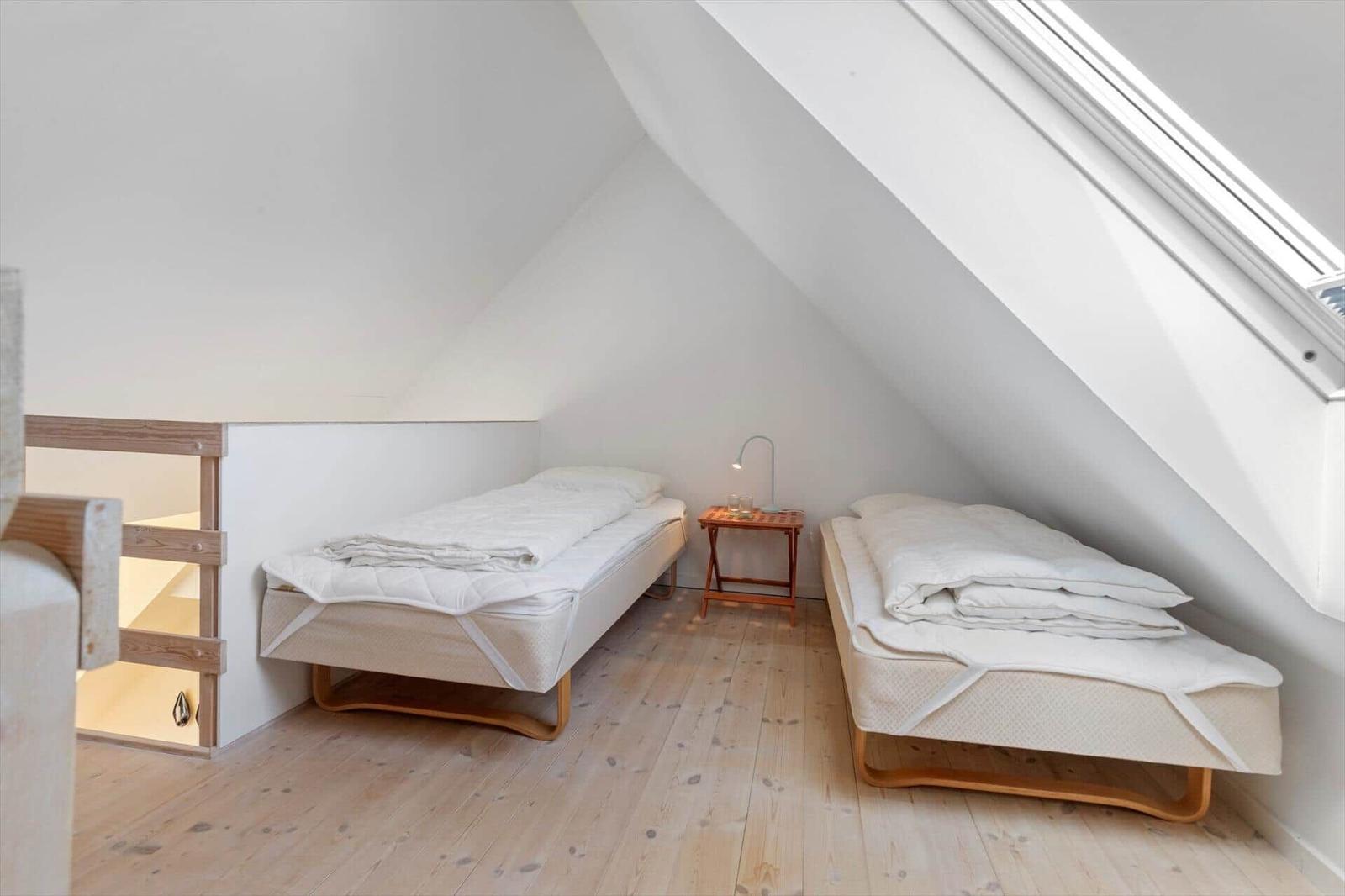 Zwei Betten in einem Dachzimmer mit Holzboden und Dachfenster.