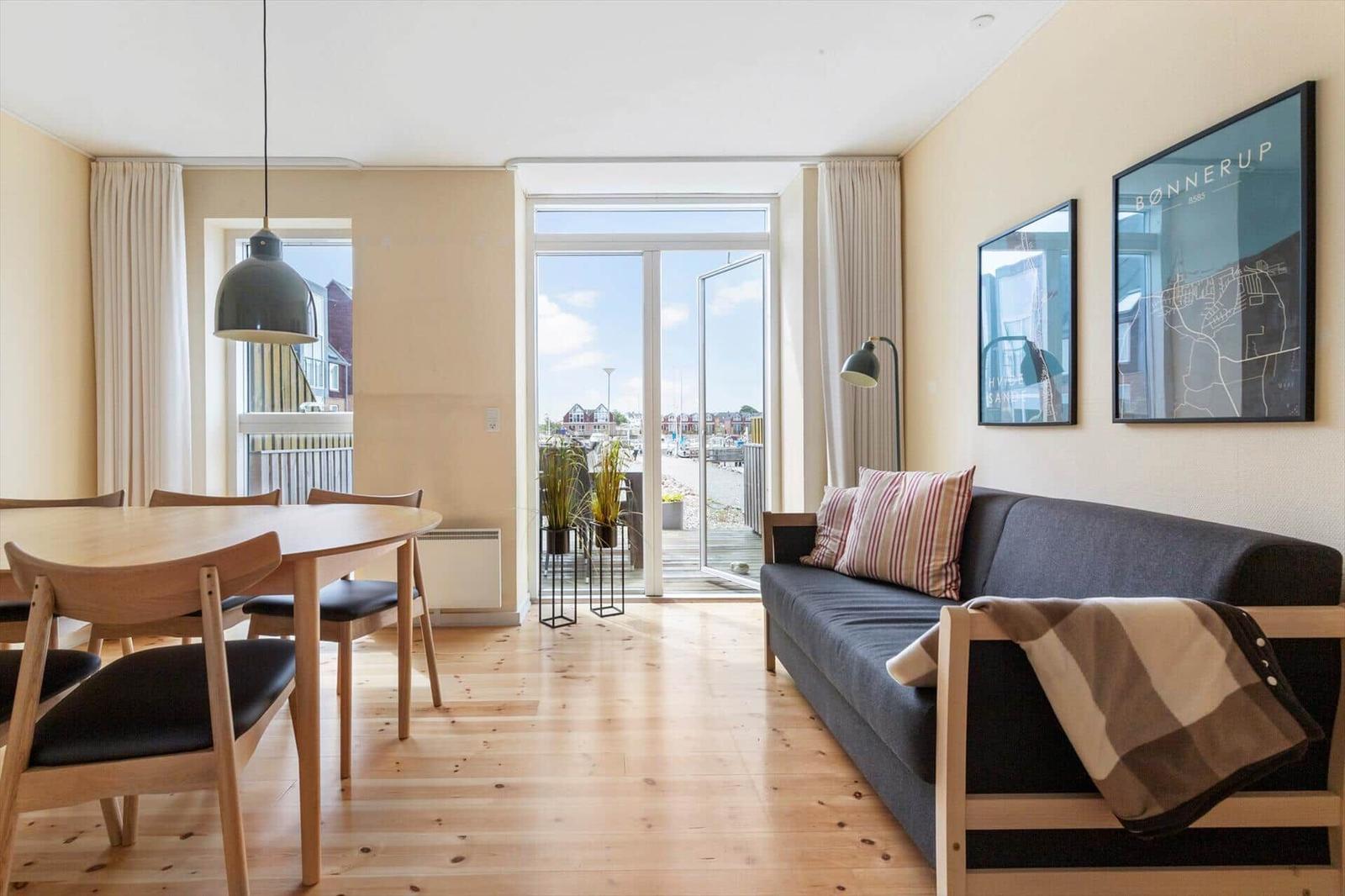 Wohn- und Essbereich mit Holzboden, Sofa, Tisch und Blick auf den Hafen.