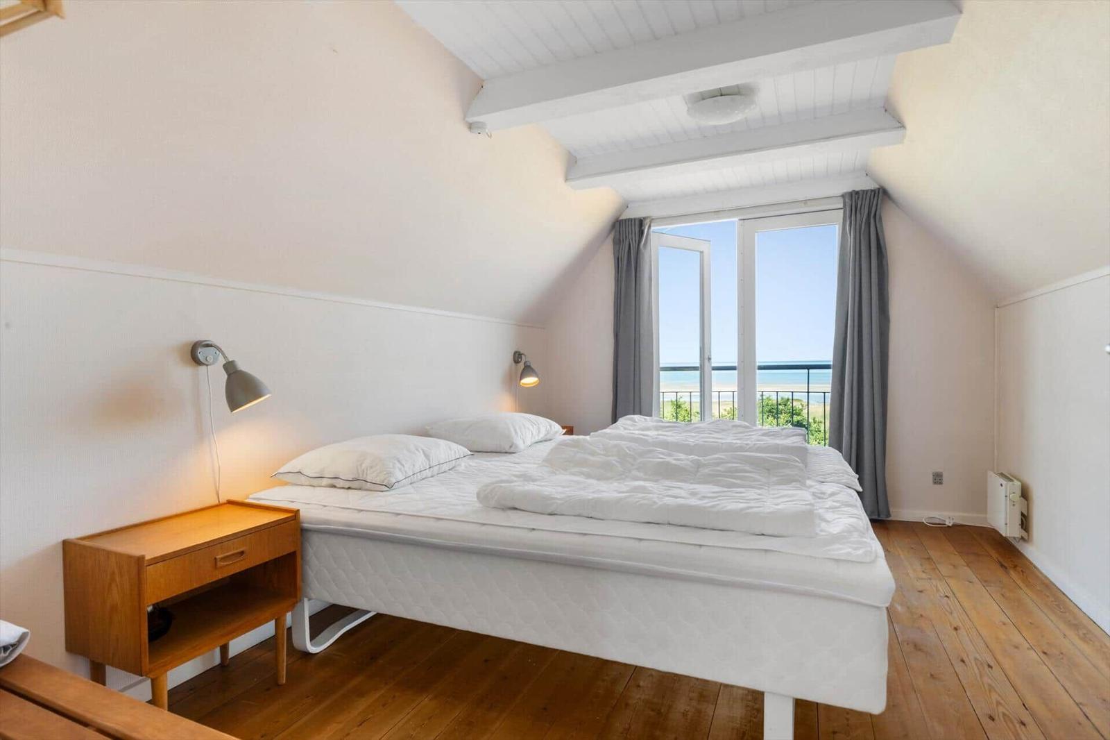 Schlafzimmer mit Blick aufs Meer, Holzboden und weißem Bett.