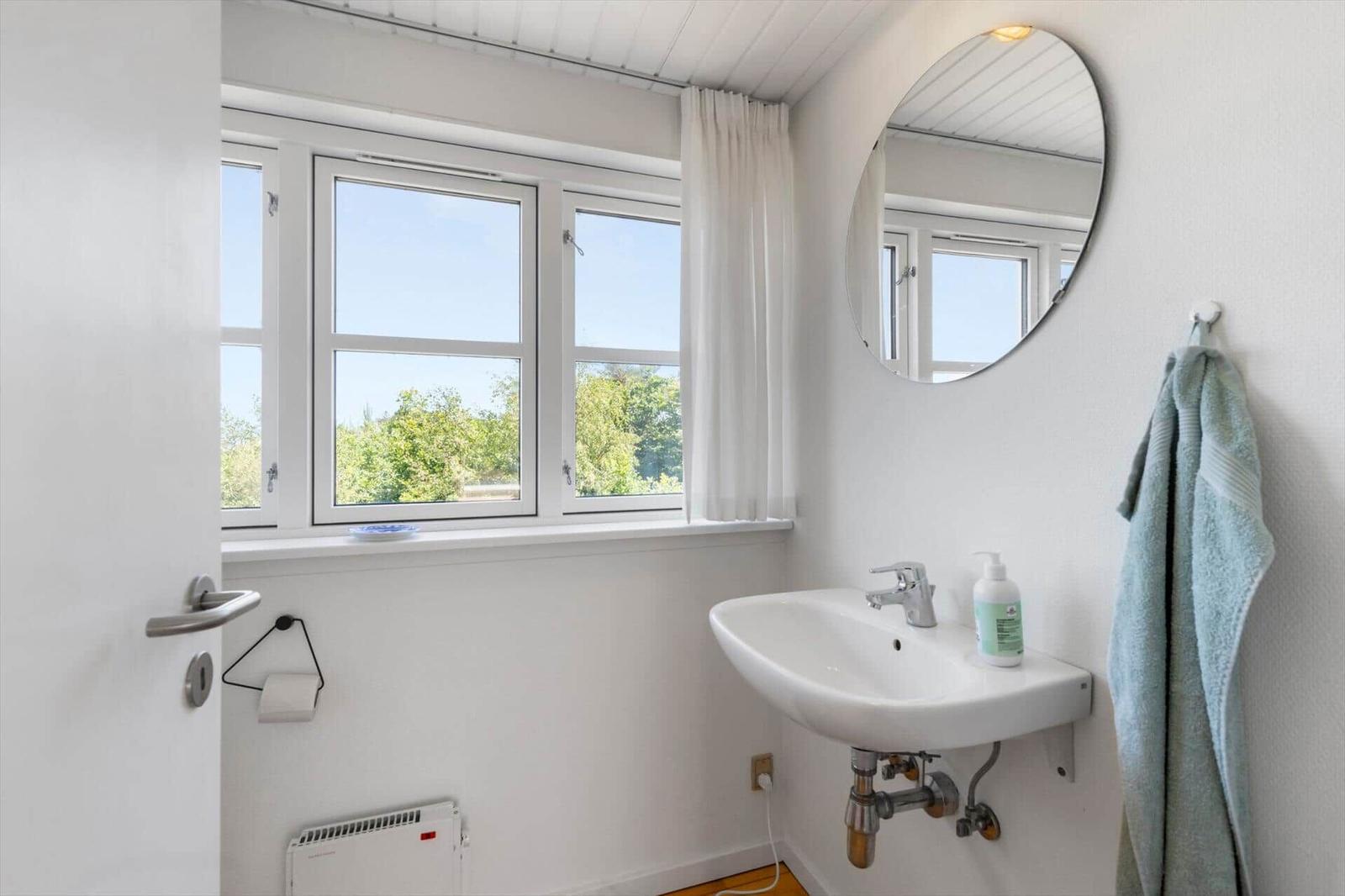 Badezimmer mit Waschbecken, Spiegel und Fenster mit Blick auf Grün.