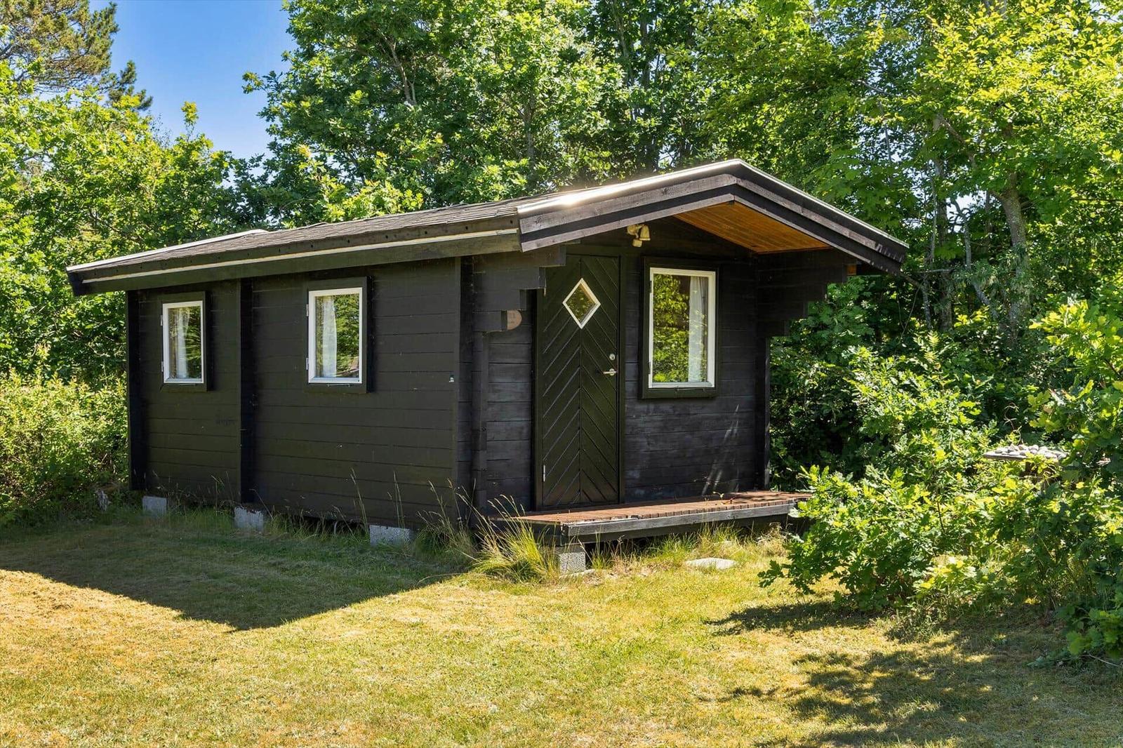 Ein dunkel lackiertes Holzhaus mit weißen Fensterrahmen und einer kleinen Veranda.