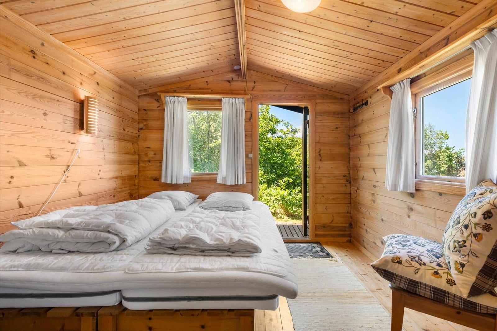 Ein Schlafzimmer mit Holzwänden, Bett und Fenster zum Garten.