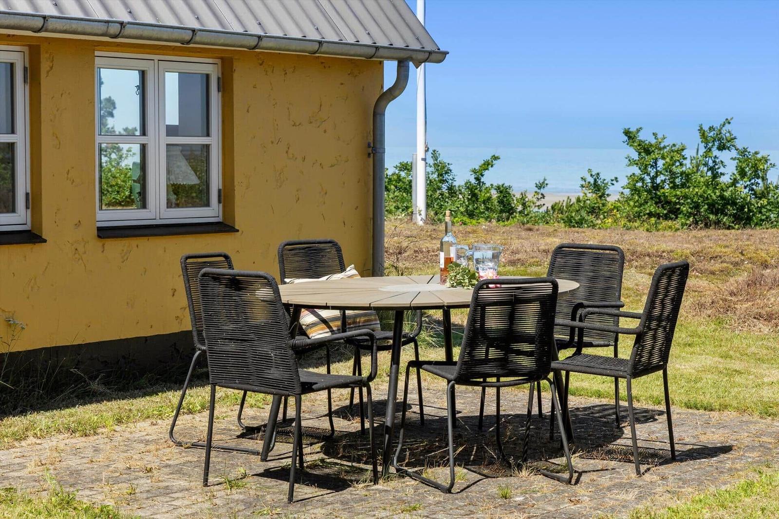 Außenbereich mit Tisch und Stühlen vor gelbem Haus mit Meerblick.