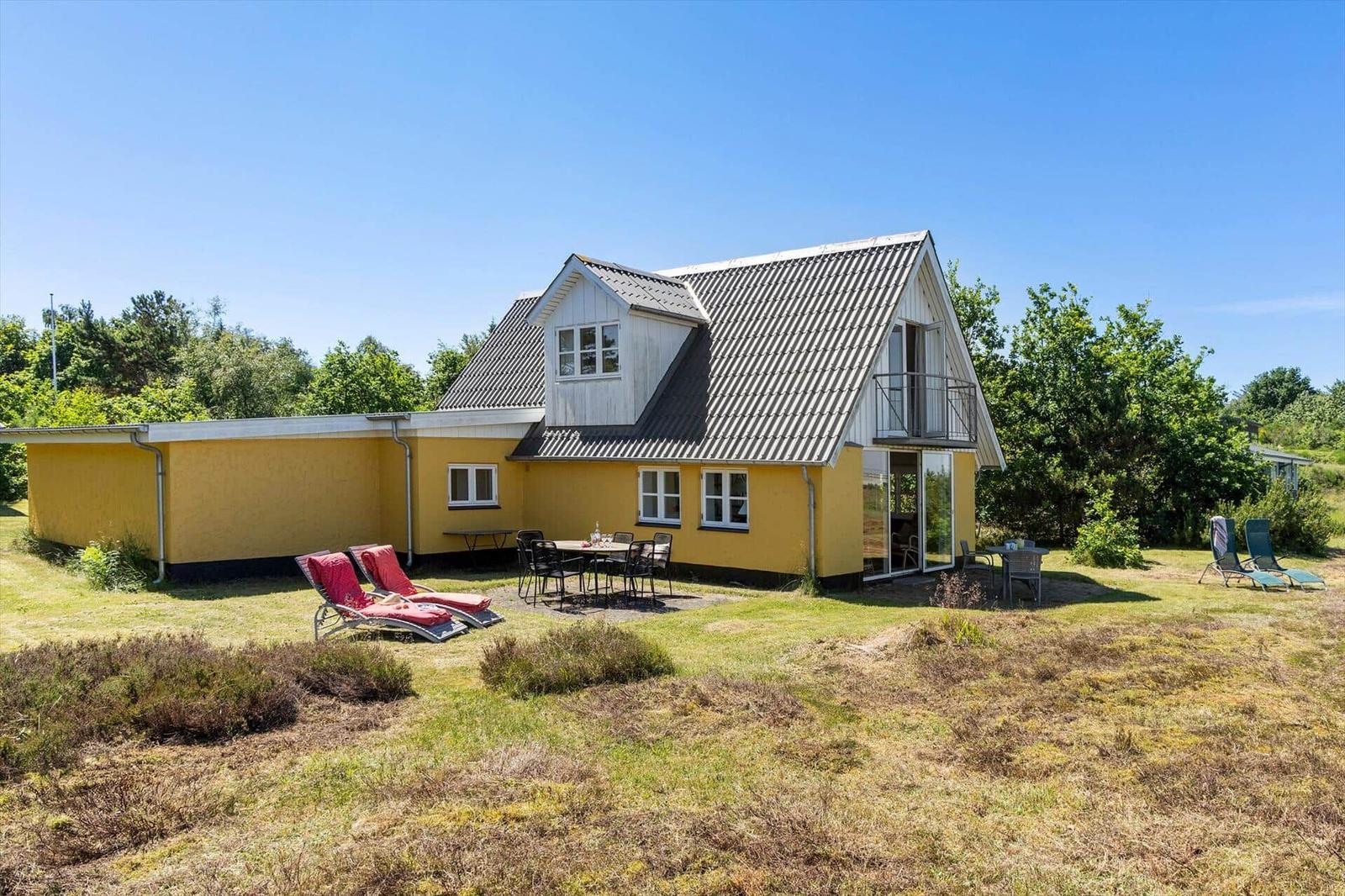 Ein gelbes Haus mit Terrasse und Liegestühlen in einer grünen Umgebung.