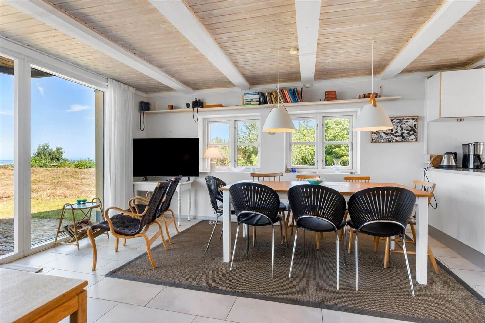 Wohn- und Essbereich mit Holzdecke, TV, Esstisch und Blick auf die Landschaft.