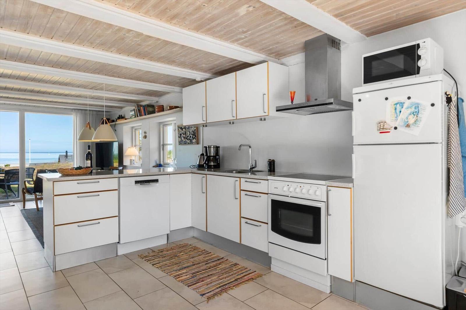 Küche mit weißen Schränken, Kühlschrank und Blick aufs Meer.