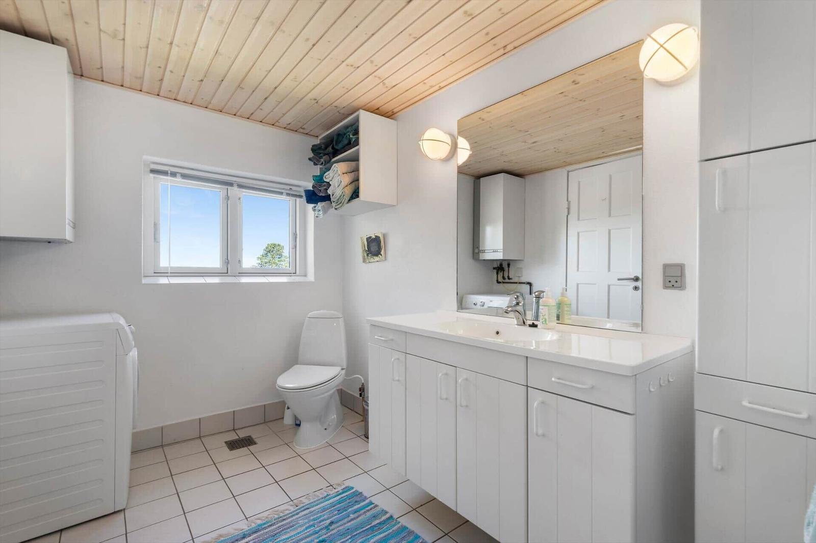 Badezimmer mit Waschbecken, Toilette und Fenster. Holzdecke und weiße Schränke.