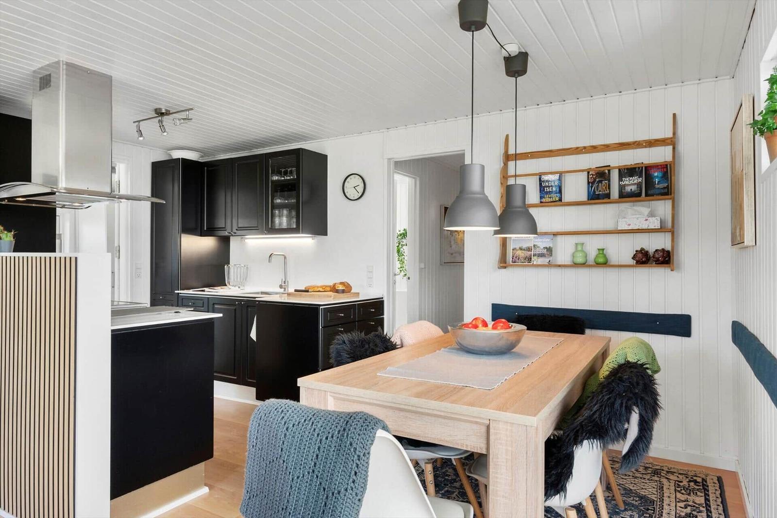 Kitchen with dining area, black cabinets, wooden table, and pendant lamps.