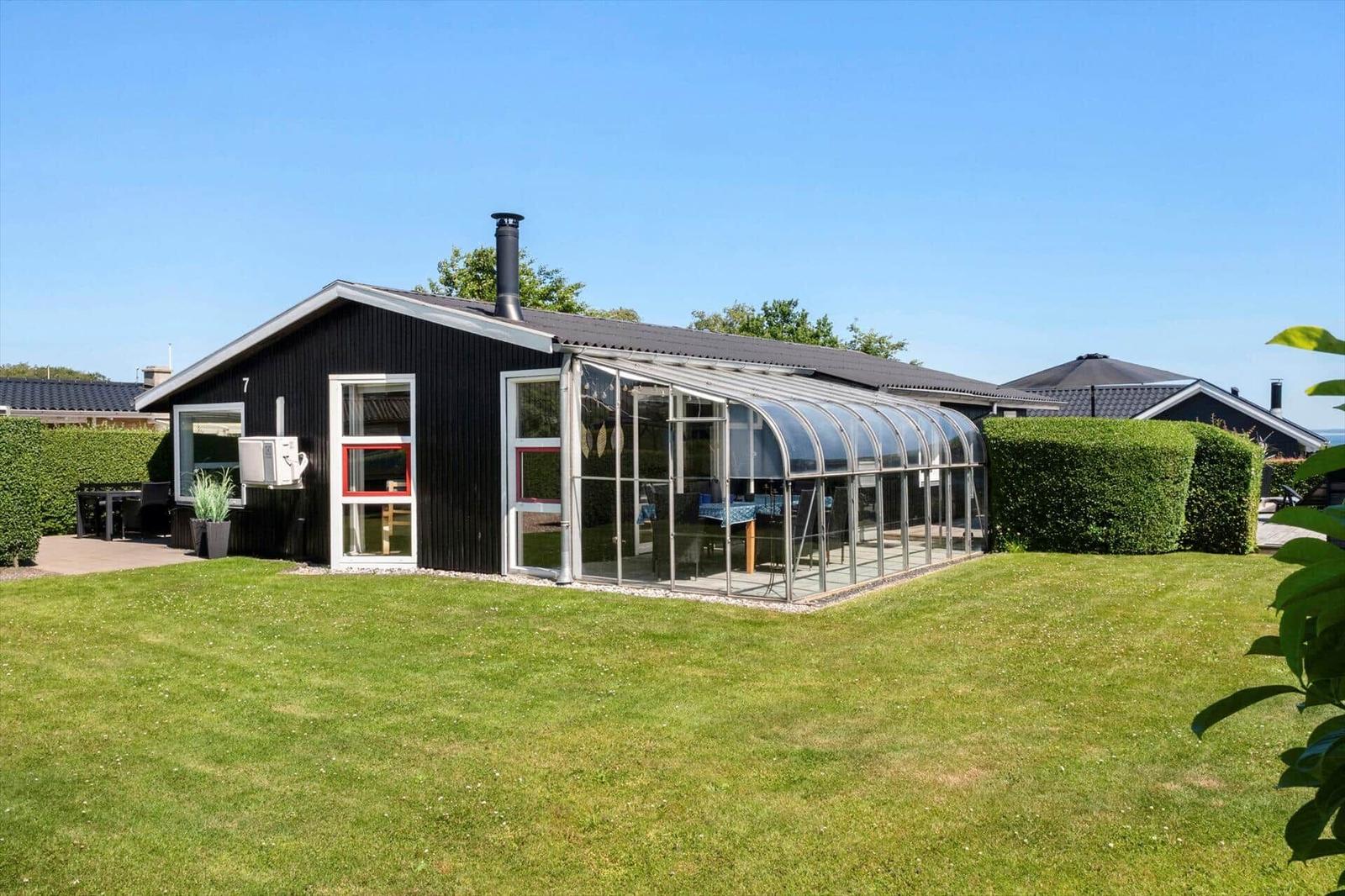 Black house with glass conservatory, green lawn, and hedges in the background.