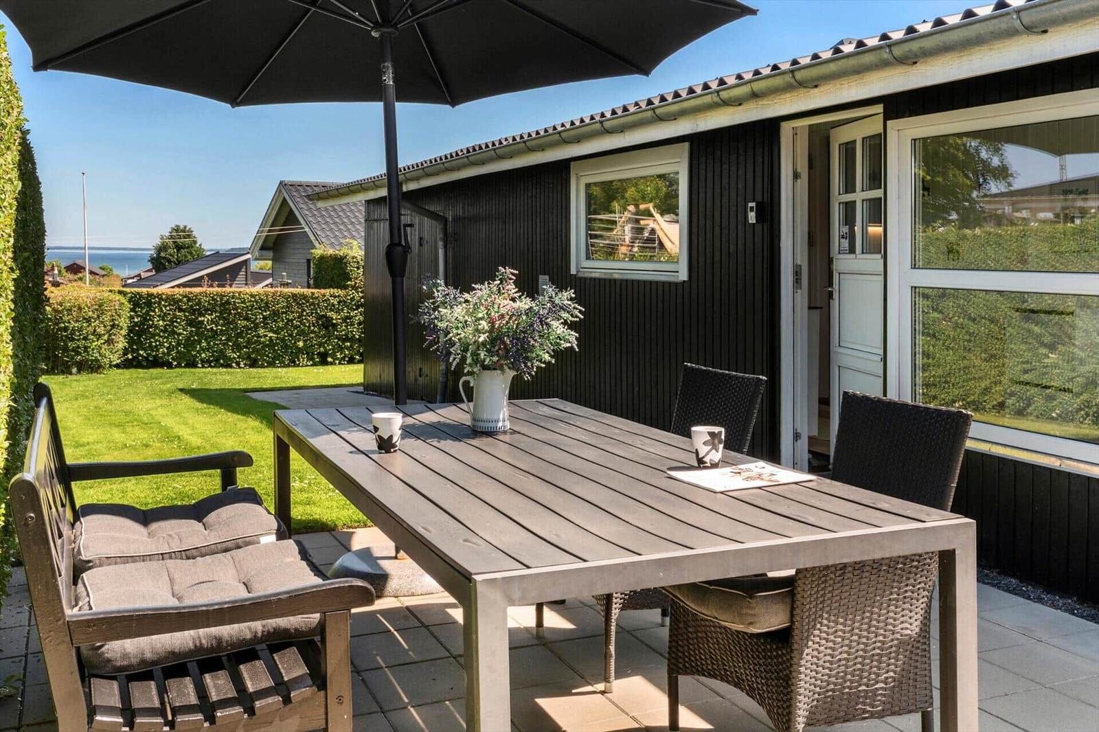 Terrace with table, chairs, and umbrella. Backyard with lawn and sea view.