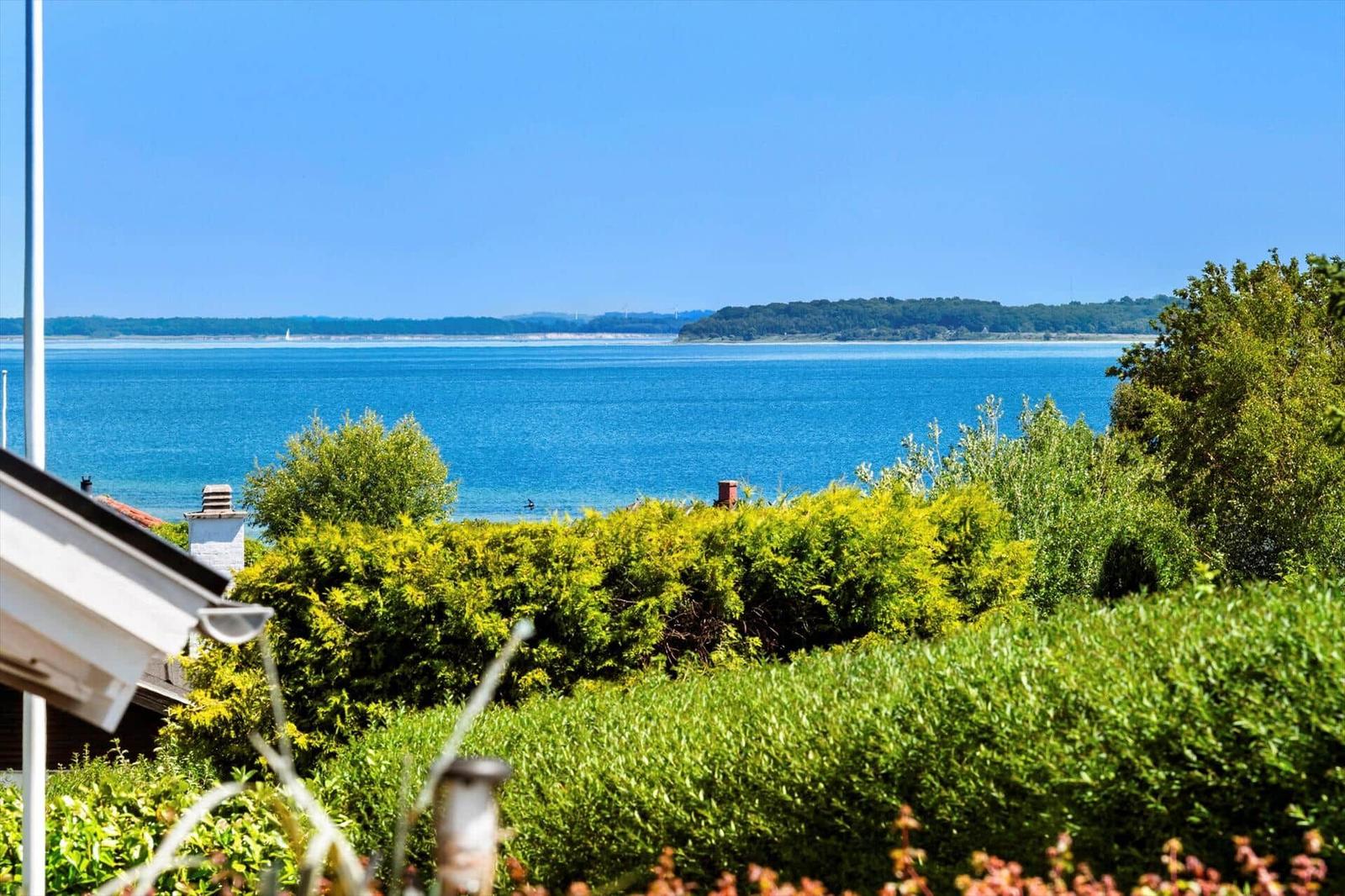 Wide view of blue water with an island in the background and green vegetation in the foreground.