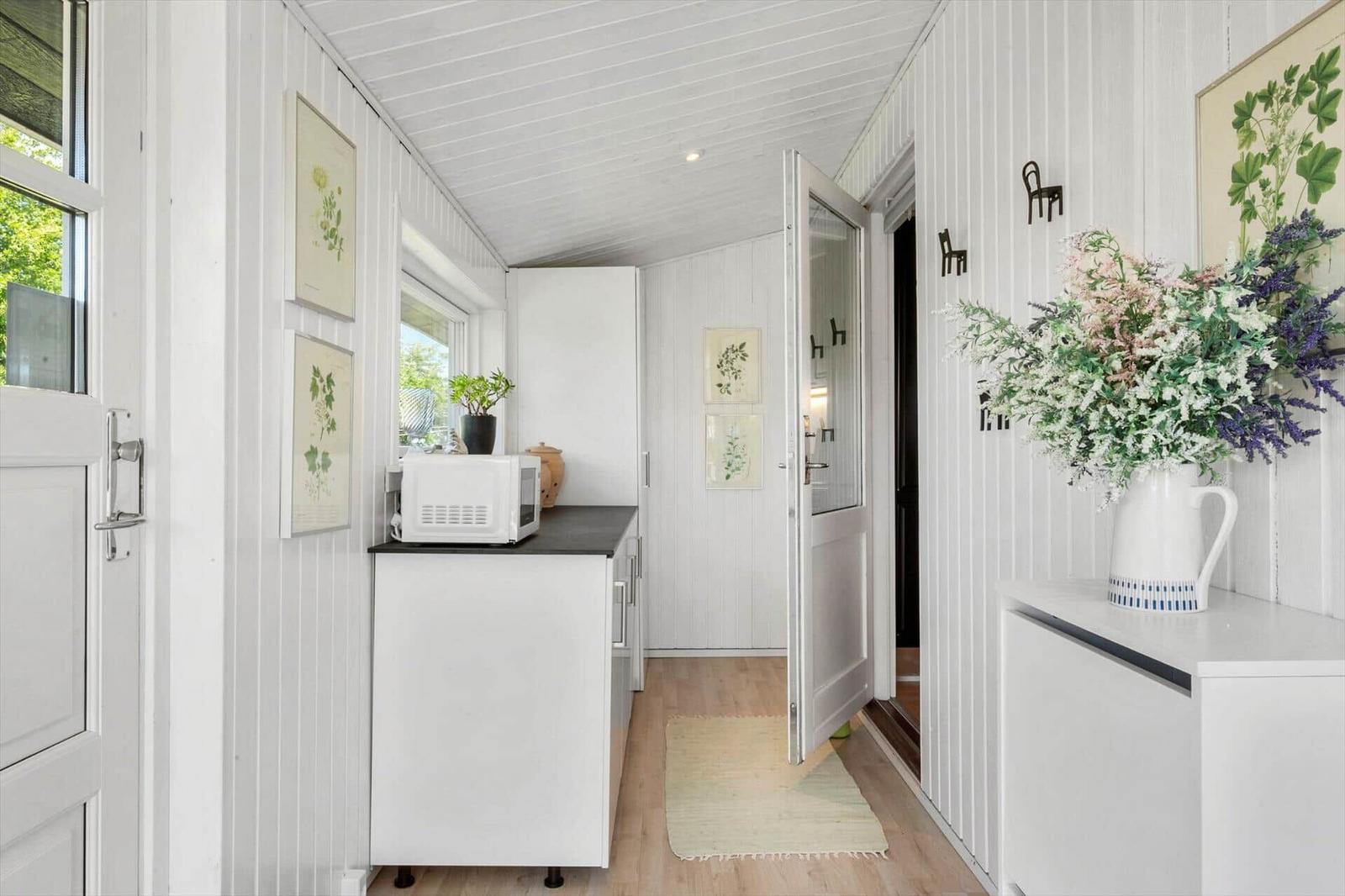 Bright kitchen with microwave and plants on walls. Wooden floor and white walls.