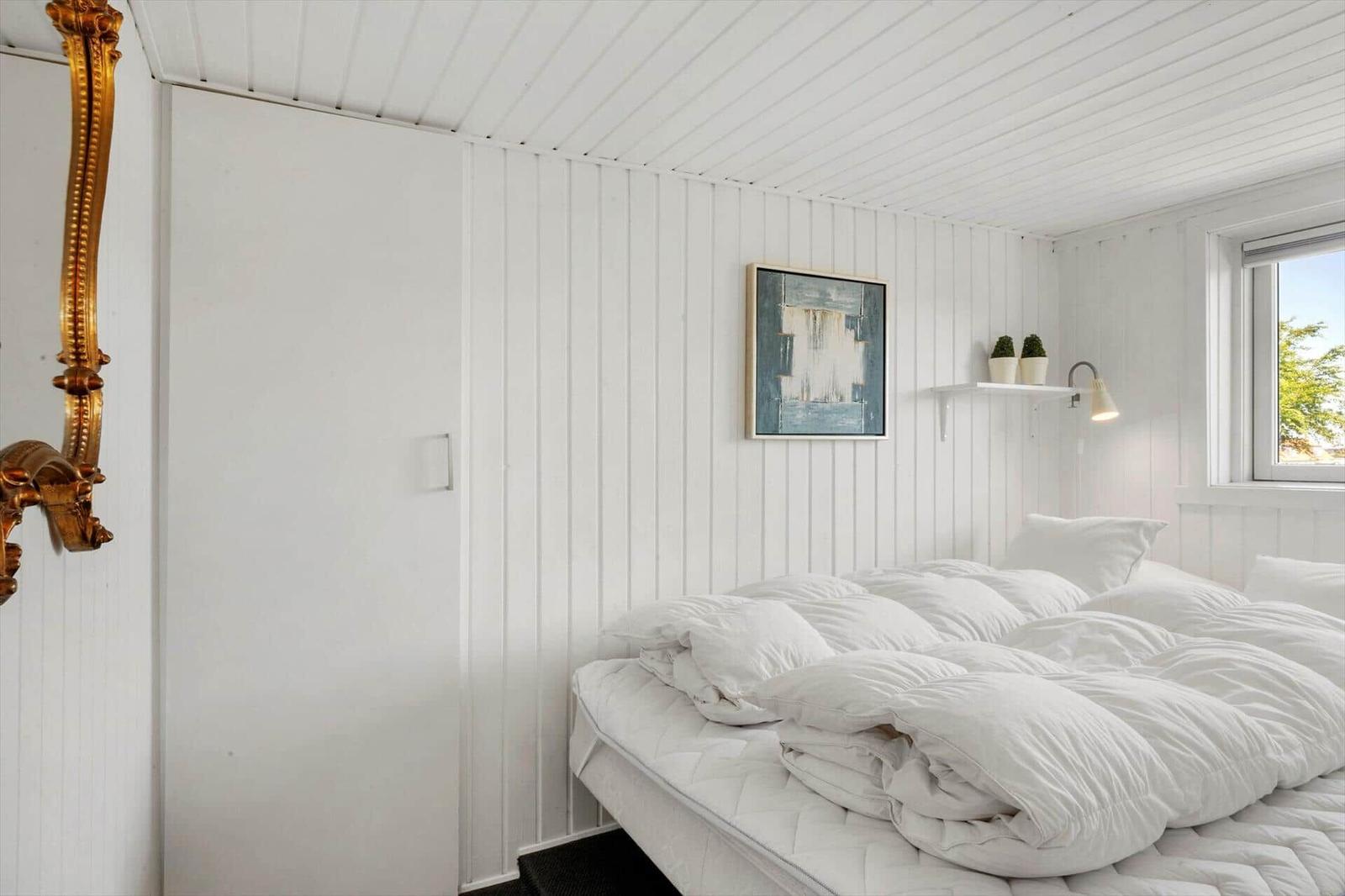 Bedroom with white bed, wall art, and window. Gold mirror on the wall.
