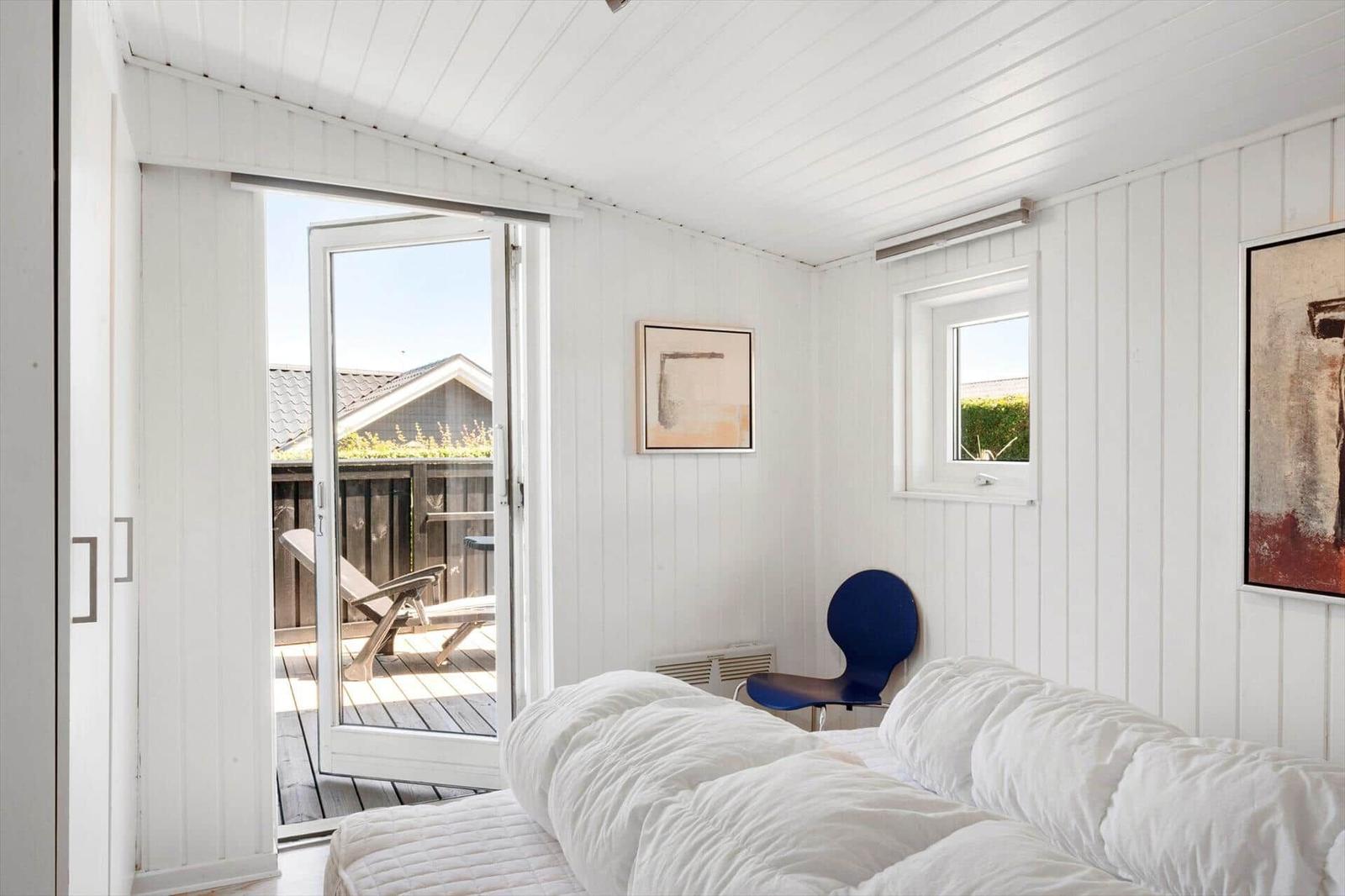 Bedroom with white walls, bed, and terrace door. Blue chair and pictures on the wall.