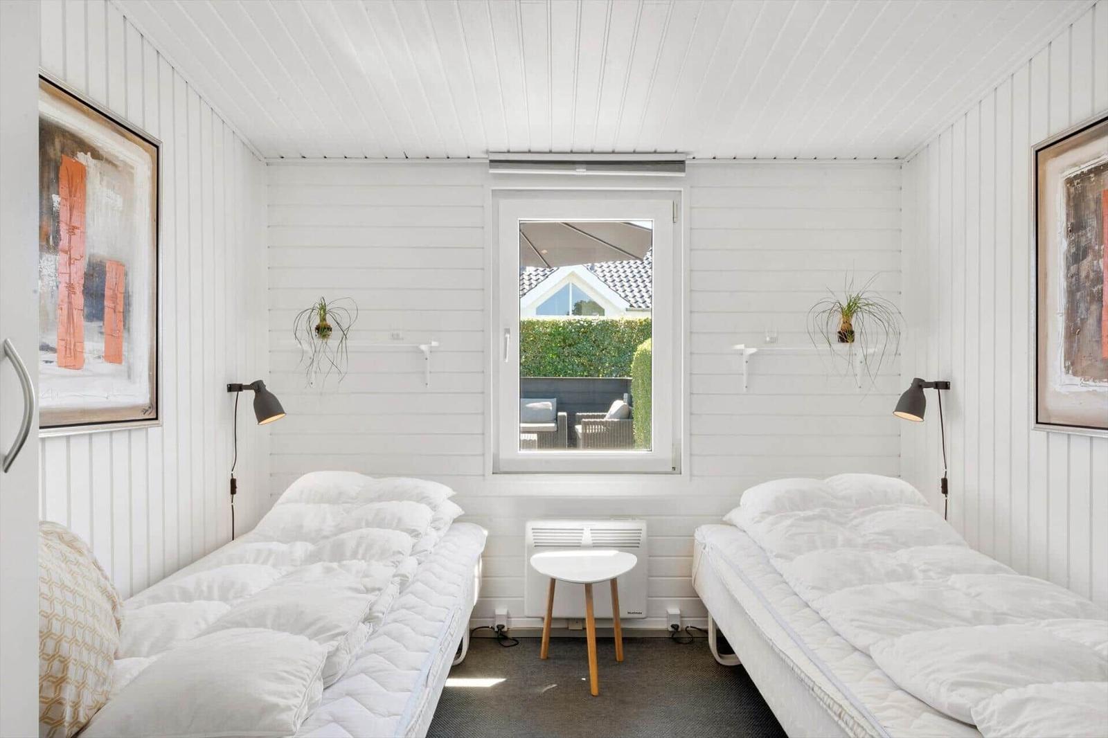 Two beds with white bedding, window overlooking garden, wall lamps and artwork.