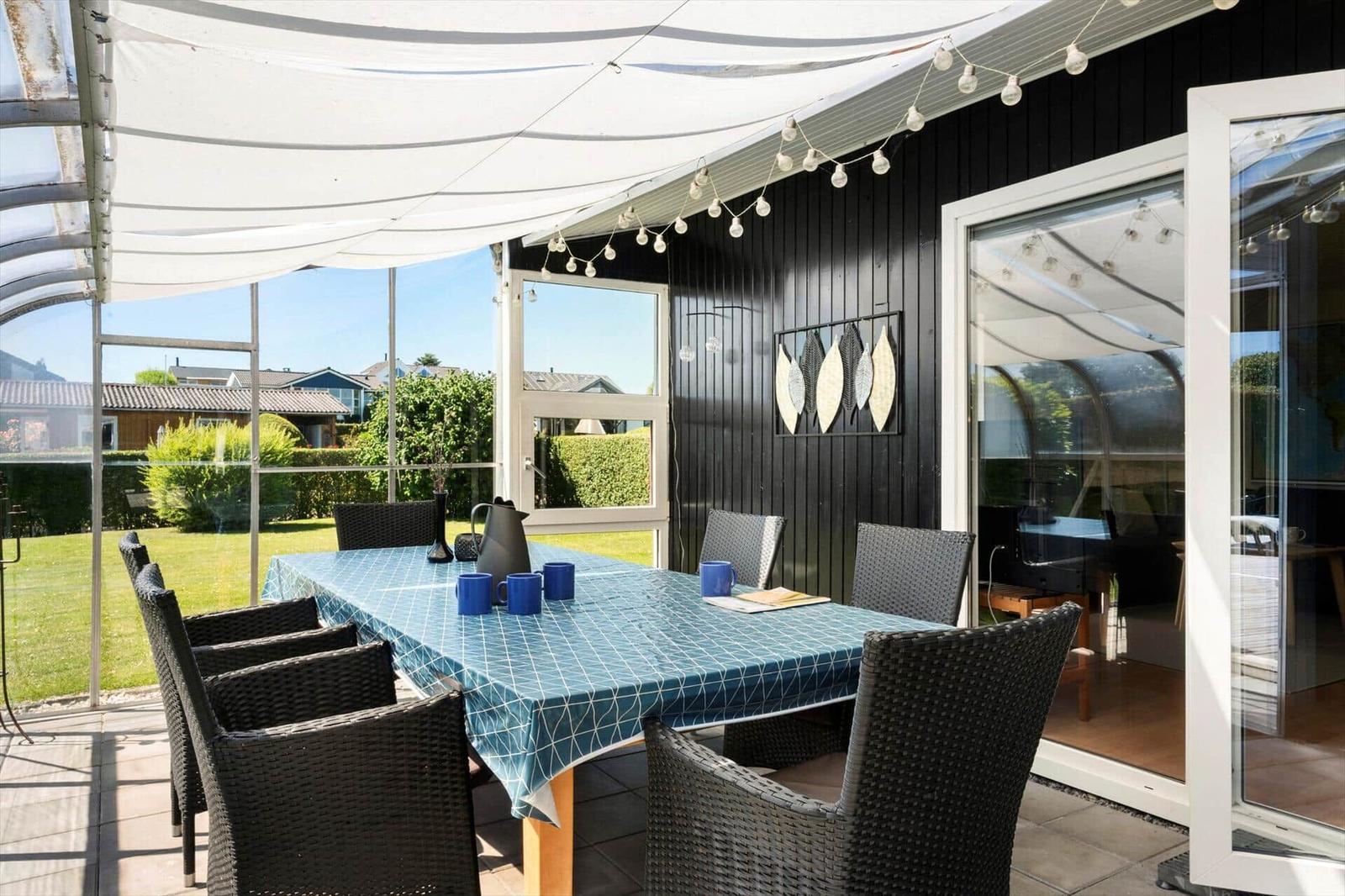 Terrace with table, chairs, and sun canopy. Background: garden and house.