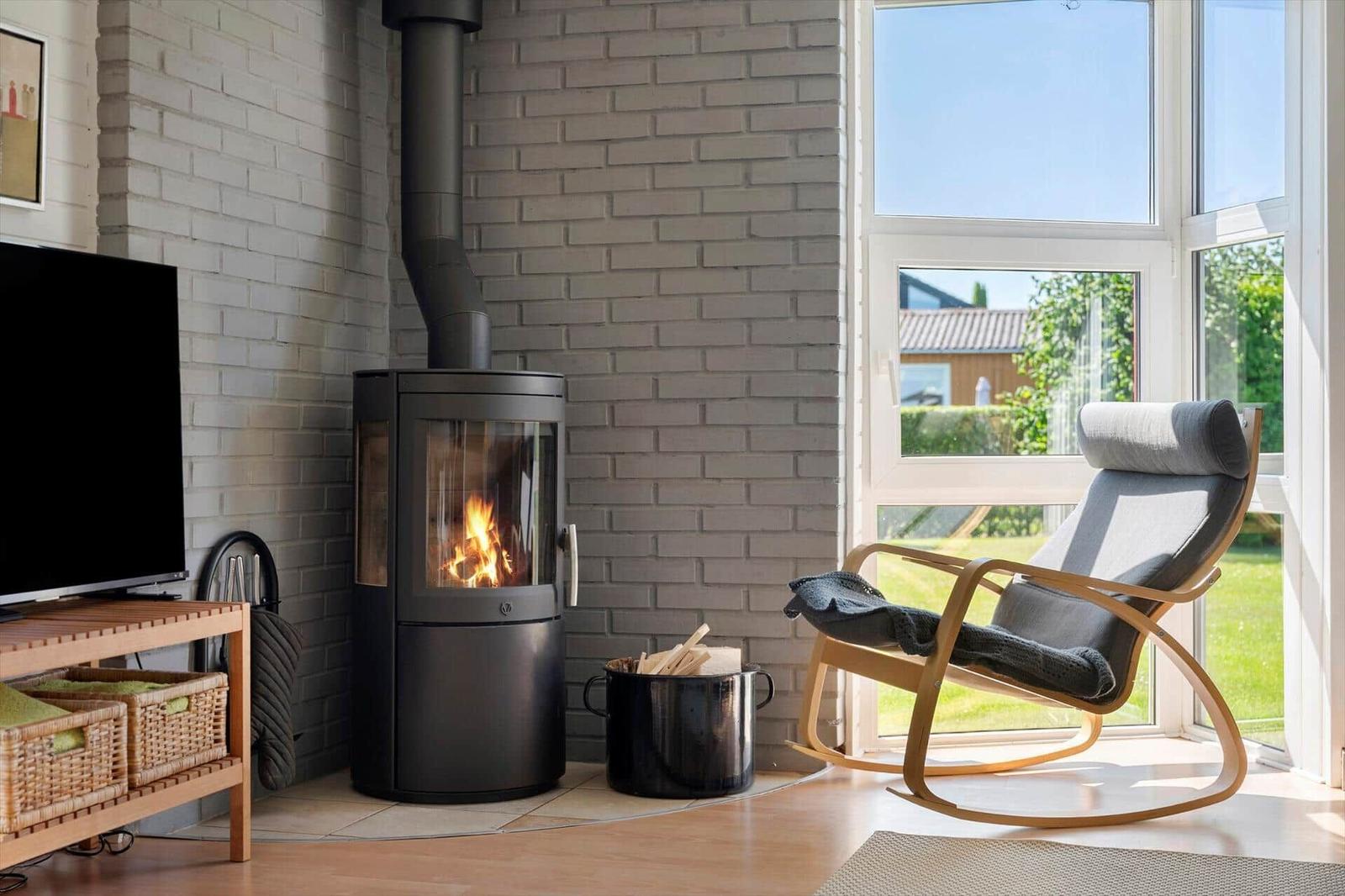 A wood-burning stove stands next to a chair by a window. A TV and a basket are also visible.