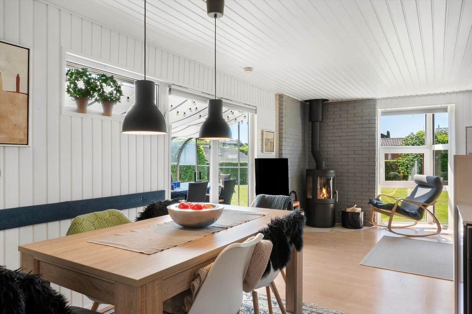 Dining room with wooden table, black pendant lights, and fireplace. Outside green area and seating.