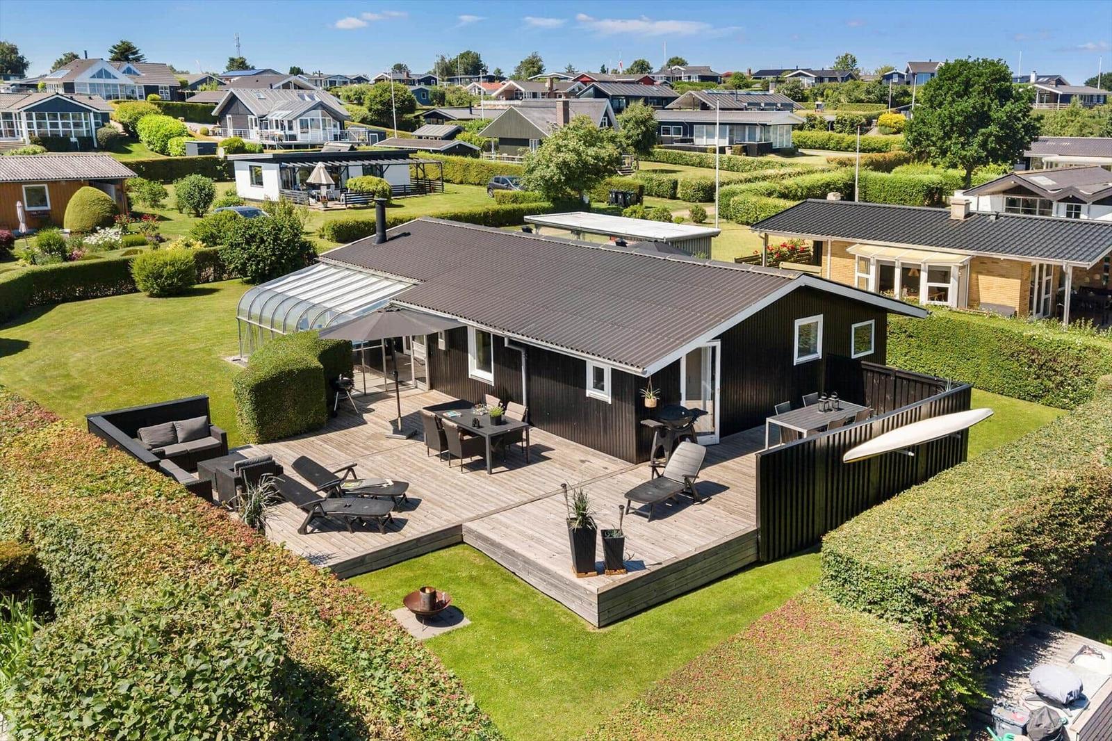 Modern villa with large wooden terrace, garden, and barbecue area. View of residential area.