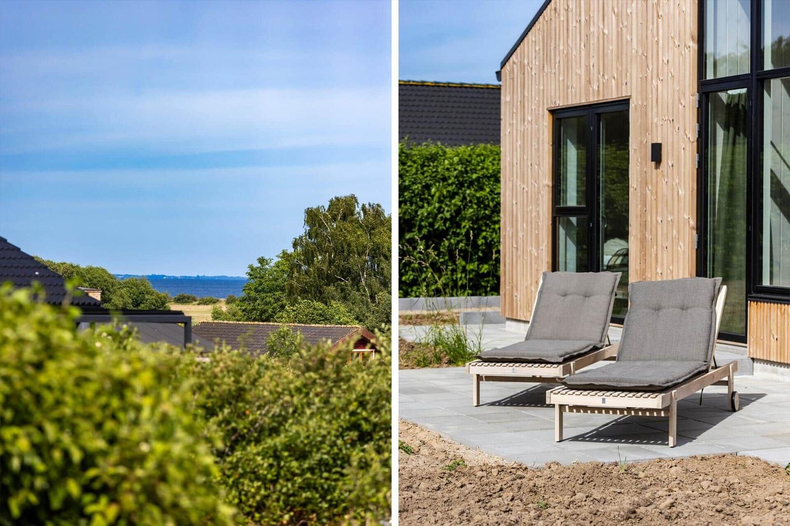 Zwei Loungemöbel stehen auf einer Terrasse vor einem Holzhaus mit großem Fenster.